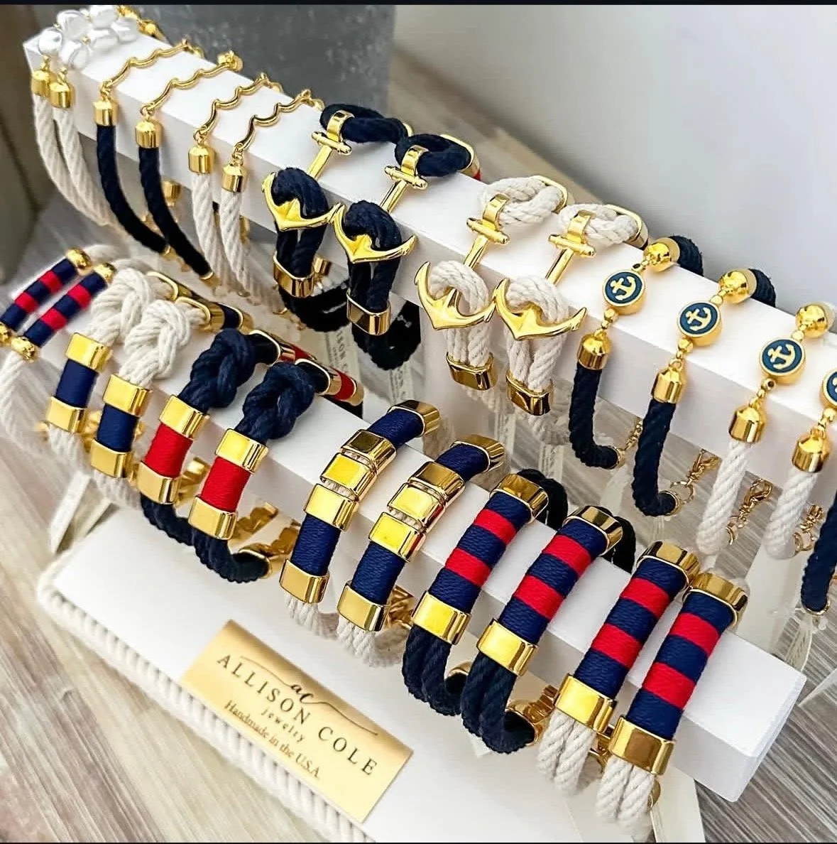 Display of various designer bracelets on white stands, including navy, red, white, black, and striped options with gold accents, by Allison Cole Jewelry.