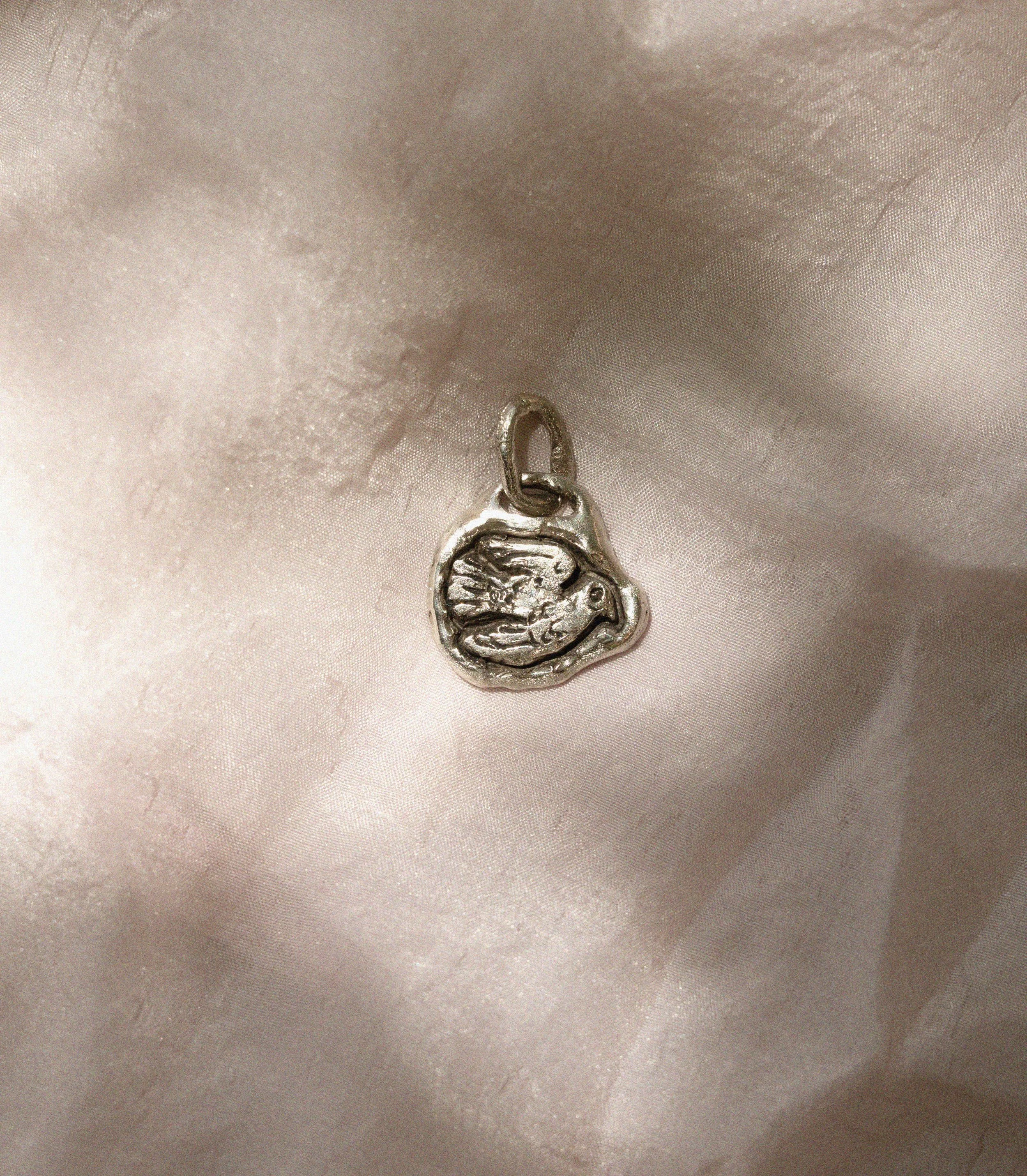 Close-up of a white gold pendant in the shape of a dove on a soft pink silk fabric.