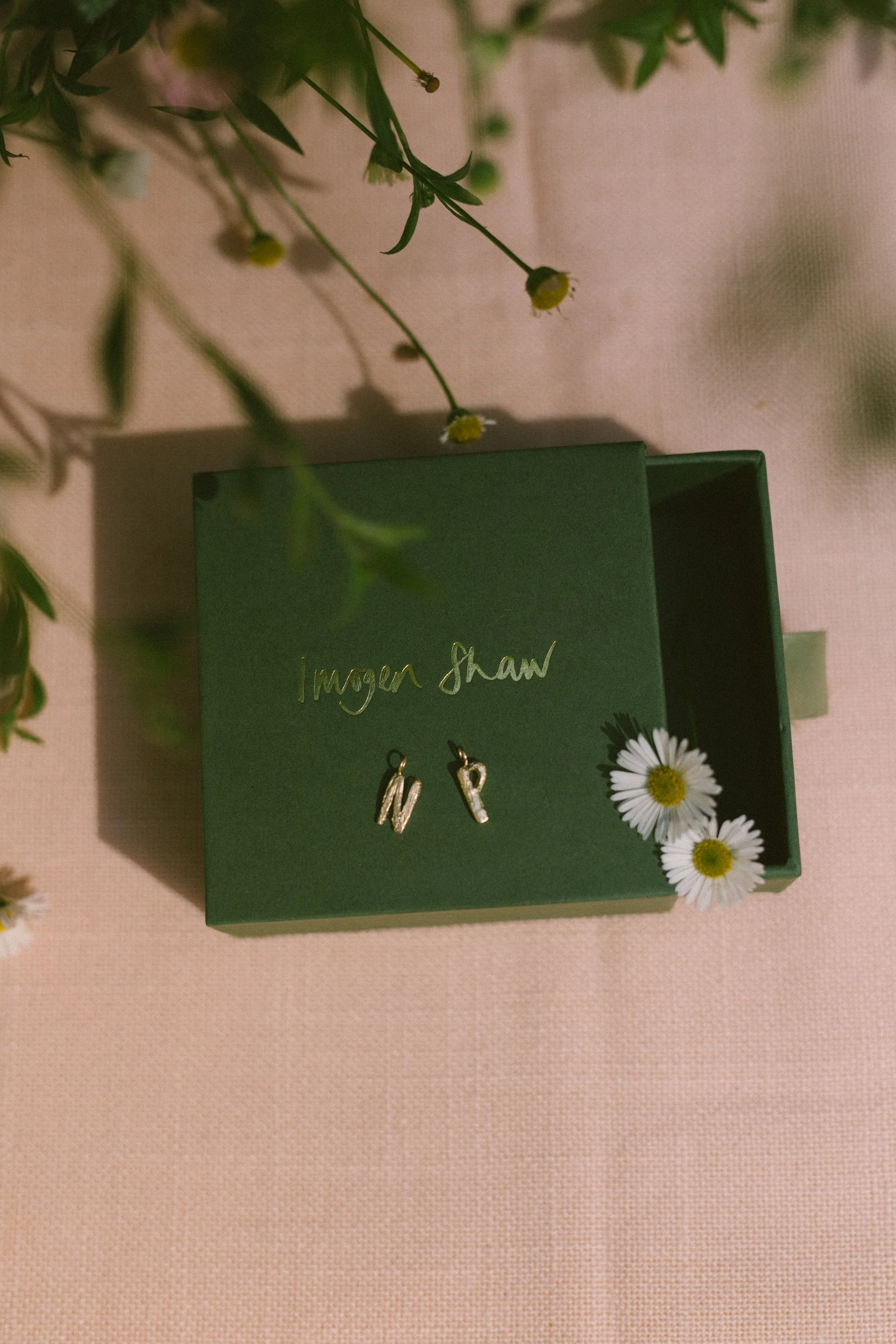 Solid gold letter charms on Imogen Shaw's green paper box with her name in gold handwriting