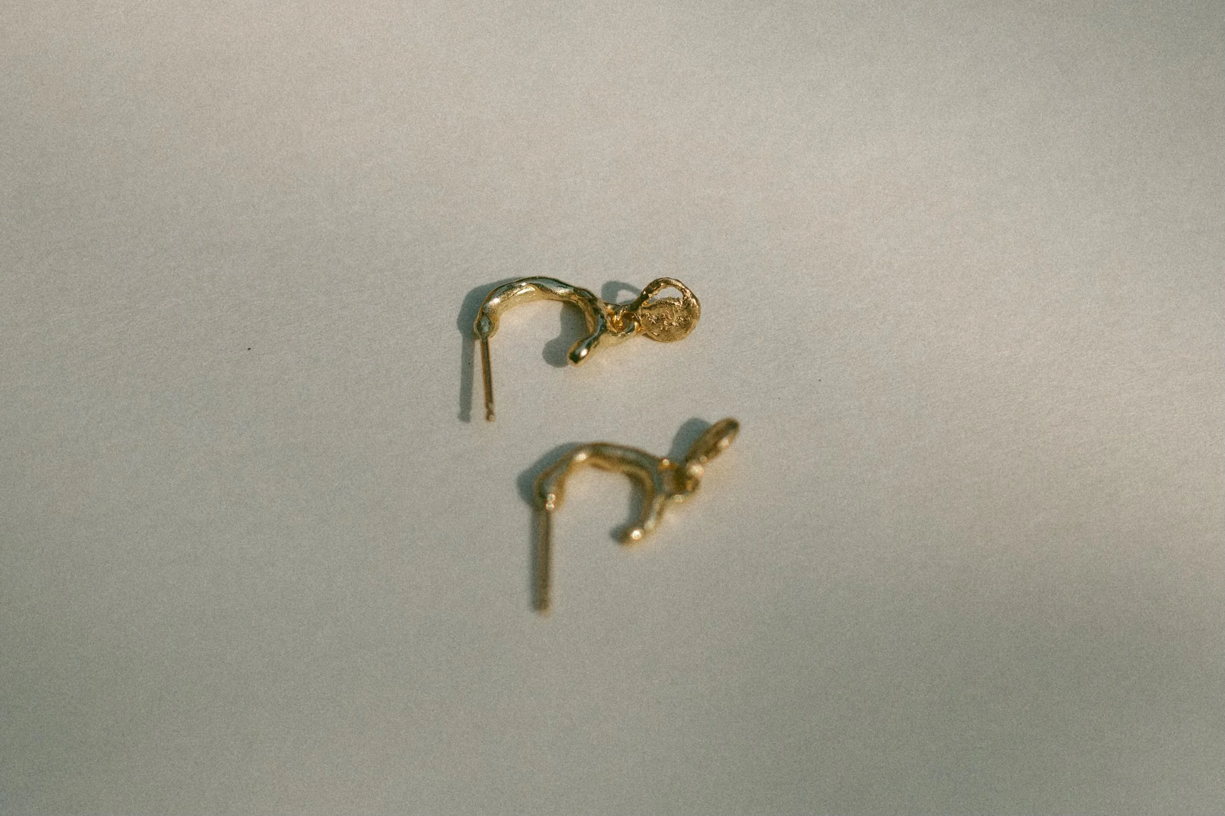 A close-up of a pair of gold hoop earrings with moon phase charms,  placed on a plain surface.