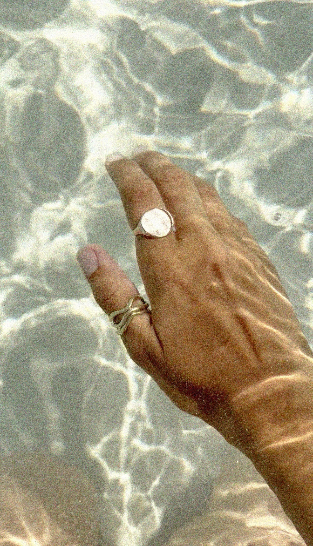 Moon phase ring in rose gold and yellow gold surrender rings on her tanned hand in clear turquoise water.