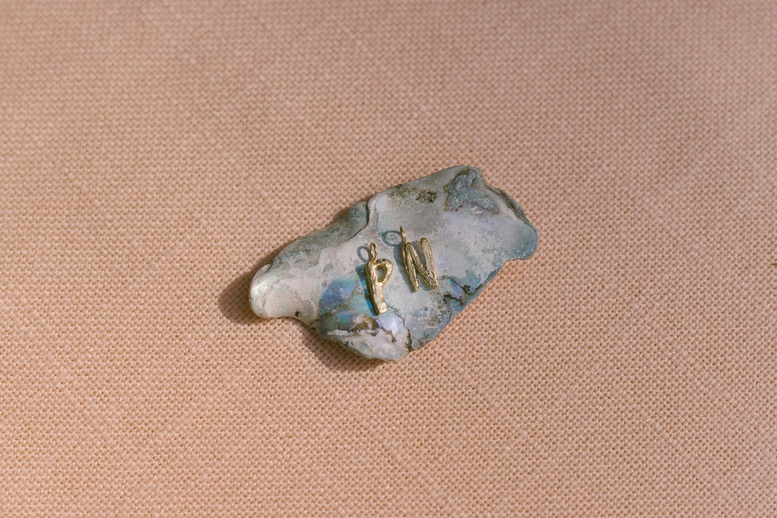 P and N letter charms positioned on a shell on a pink linen cloth