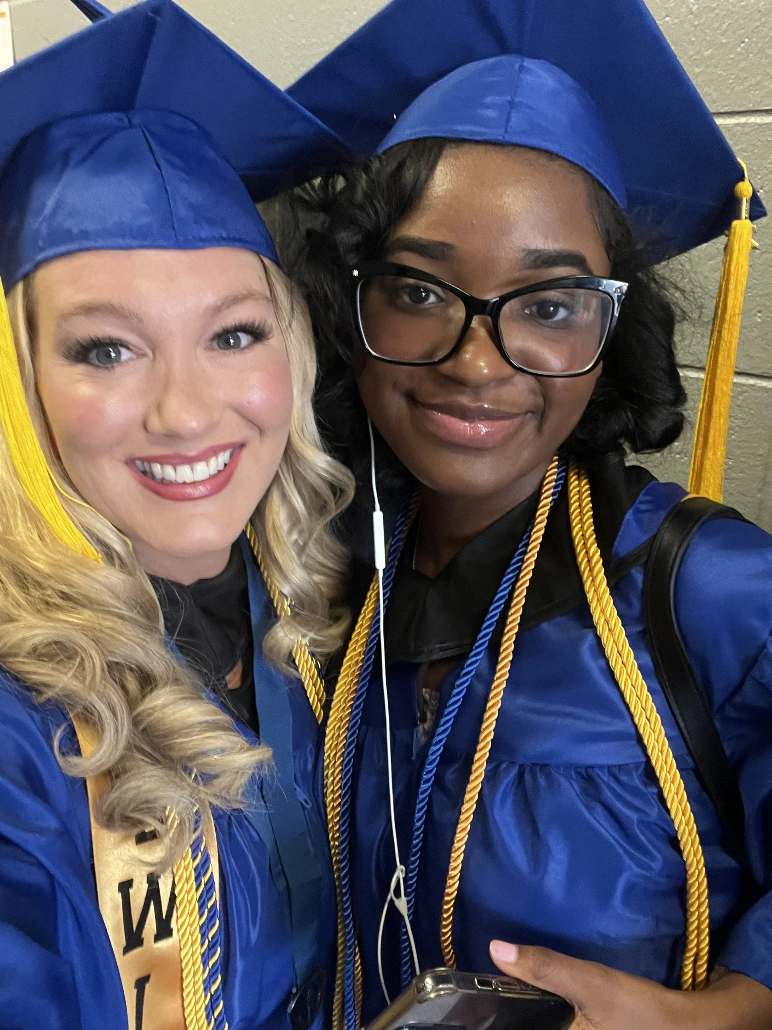 Two women in blue graduation gowns and caps taking a selfie.
