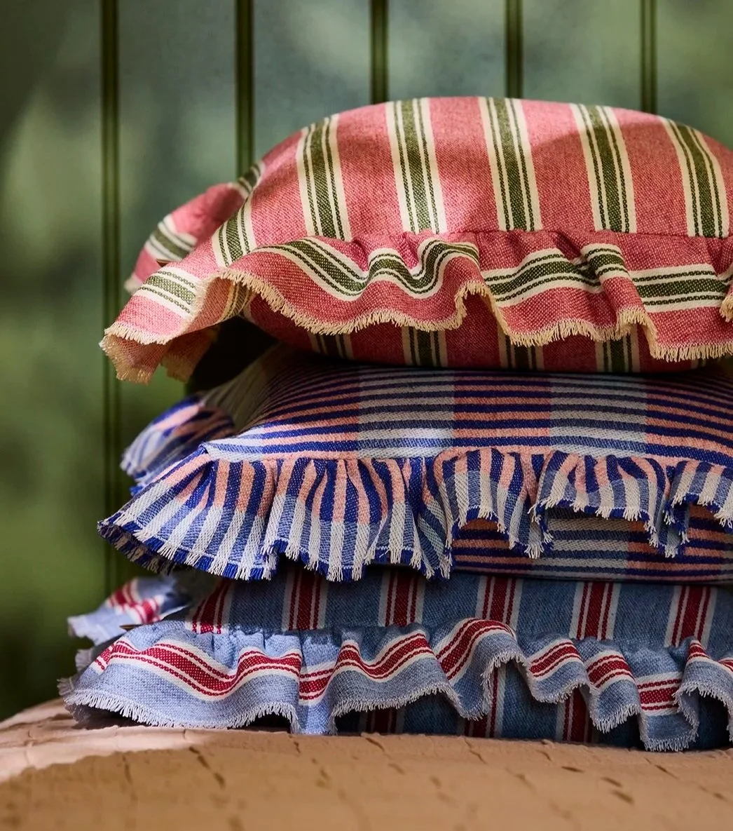 Stacked cushions with ruffled edges, in pink, blue, purple, and green patterns.