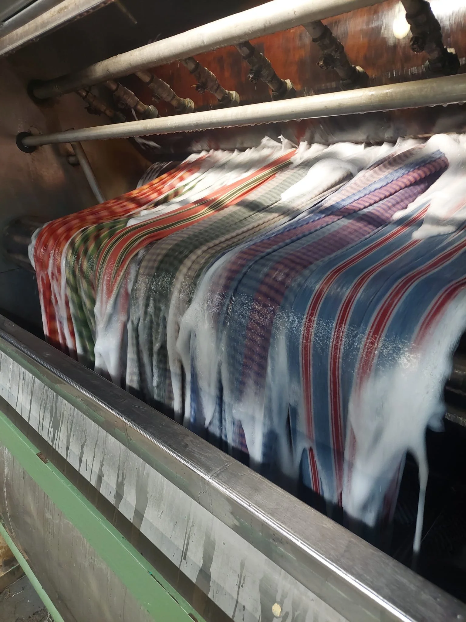 A fabric scouring machine with patterns in red, green, blue, and white, with water flowing over the fabric as part of the washing process.
