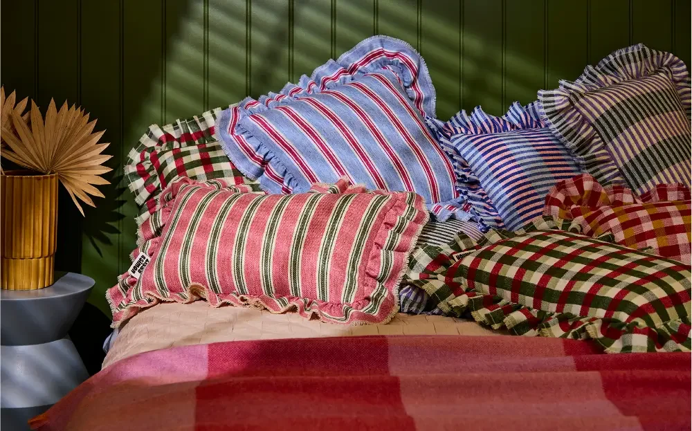 Striped and checked cushions on a bed, in front of a green panelled wall.