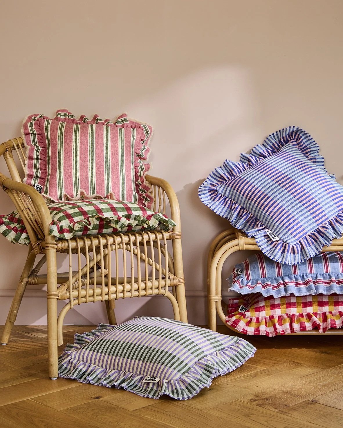 Rattan chairs with colorful striped and checkered cushions with ruffled edges, placed against a beige wall on a hardwood floor.