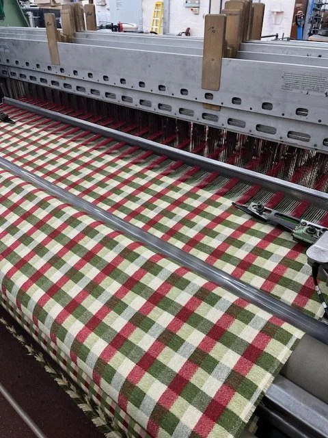 A loom weaving red, green, and white gingham fabric.