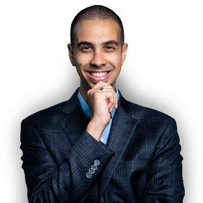 Mohammed Faris in a dark blue plaid suit with a light blue shirt, posing with his hand near his chin against a white background.