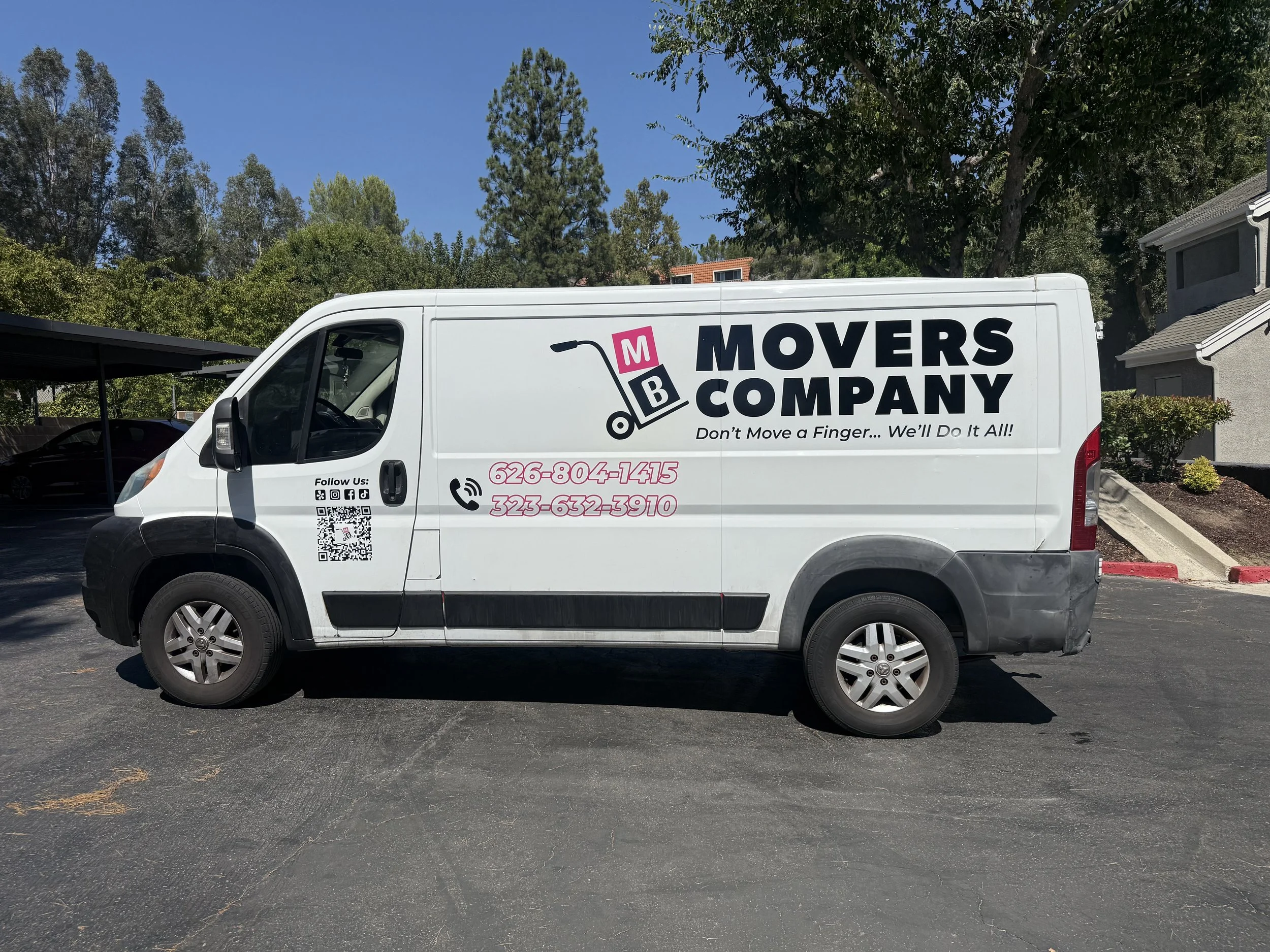 White moving company van with black and pink lettering parked on asphalt in a lot surrounded by trees and residential buildings | Grizzly Signs | Los Angeles, CA | Custom Wraps