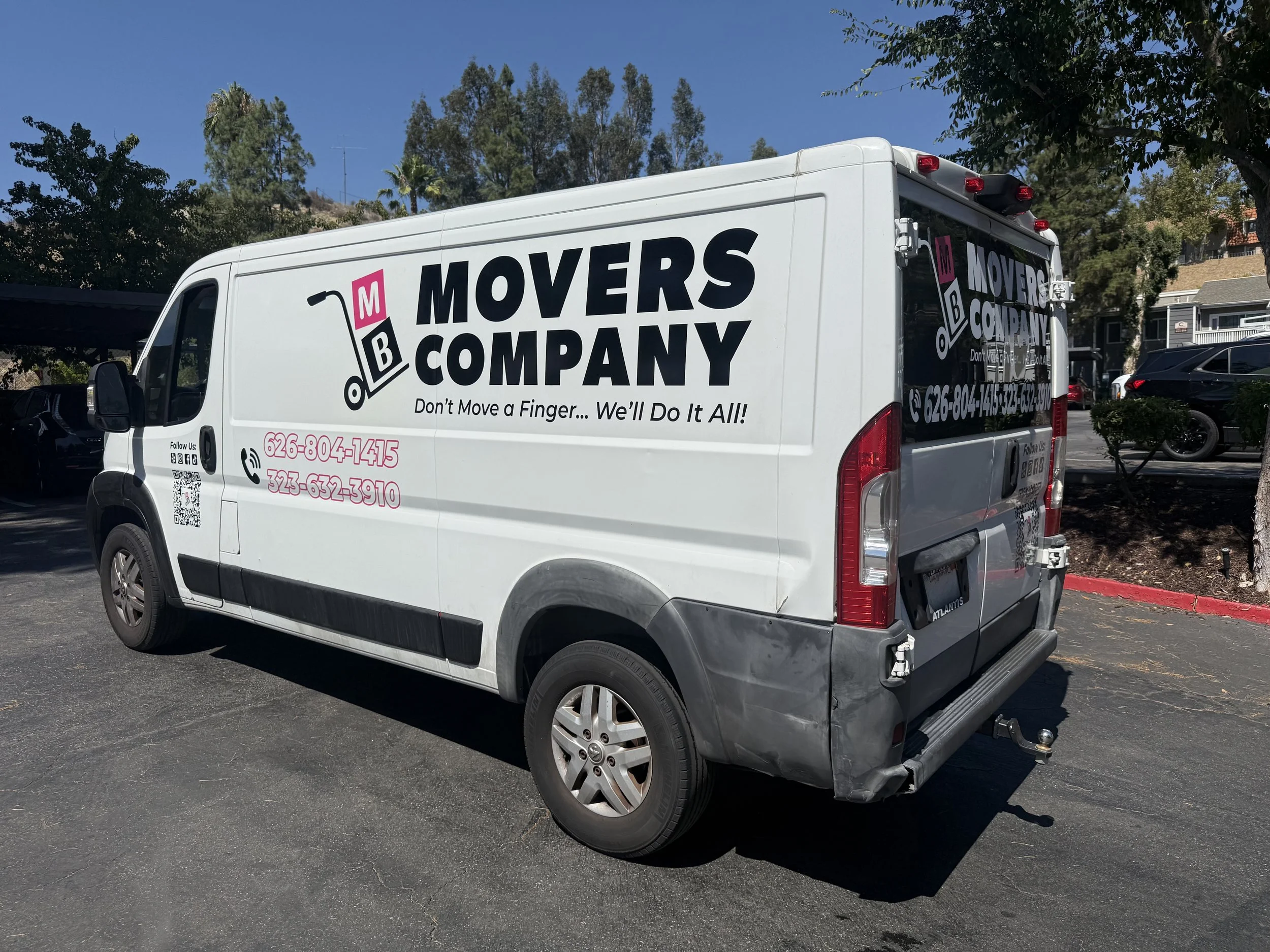 White moving truck with black and pink company logo and contact information, parked outside on a sunny day with trees and buildings in the background. | Grizzly Signs | Los Angeles, CA | Custom Wraps