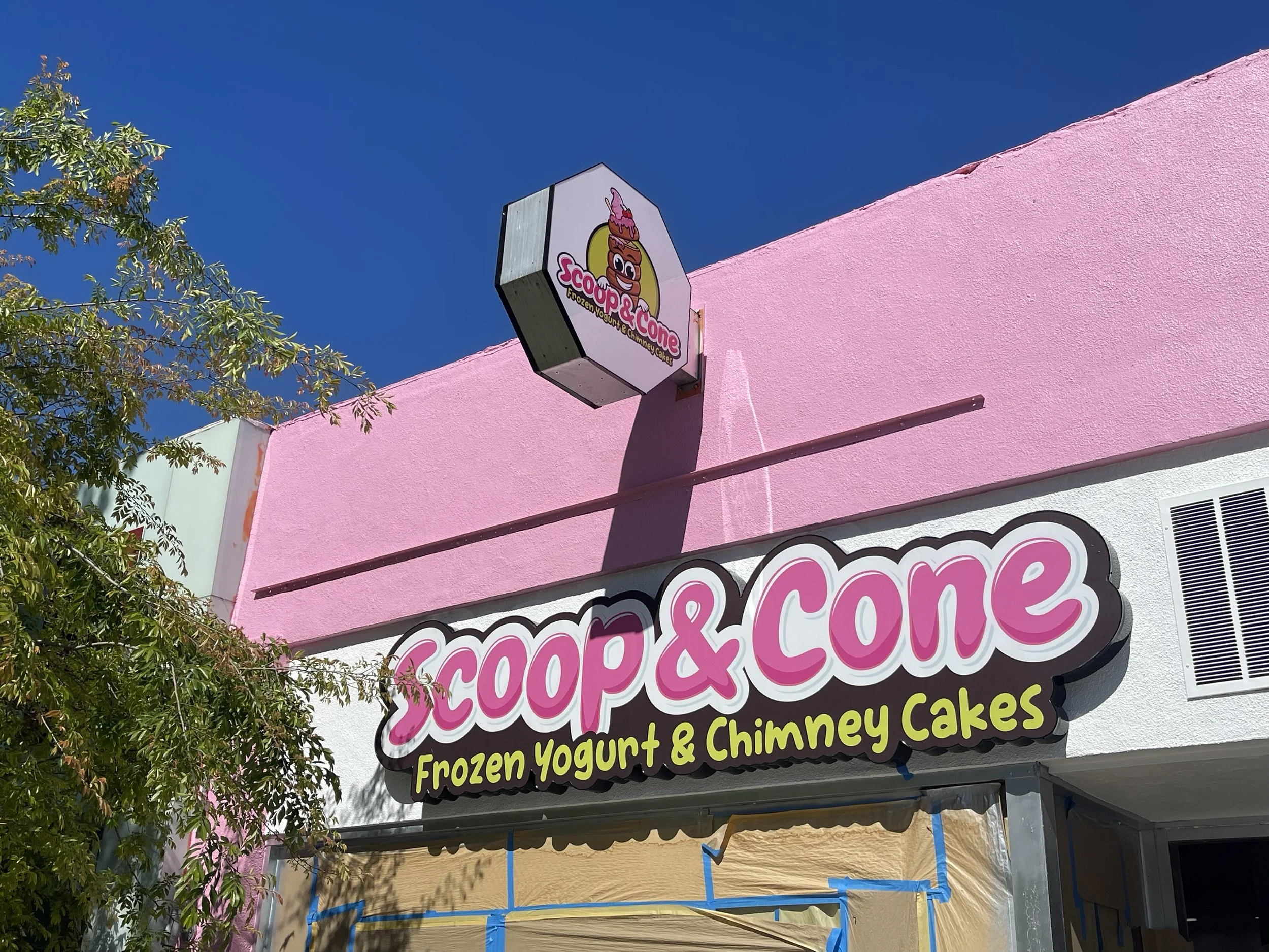 Sign for Scoop & Cone frozen yogurt and chimney cakes shop, with pink and white facade, a small logo sign above, and blue sky in the background | Grizzly Signs | Los Angeles, CA | Custom Signs