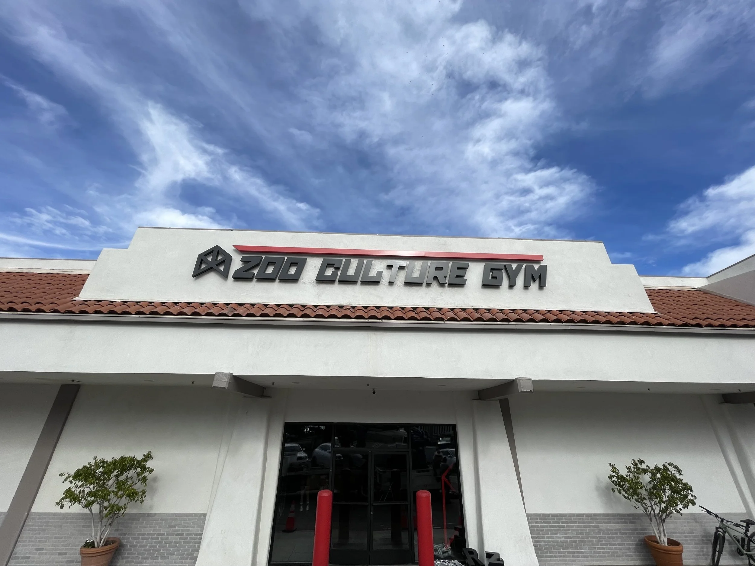Facade of Z00 Culture Gym with white walls, red-tile roof, and signage under a blue sky with clouds | Grizzly Signs | Los Angeles, CA | Custom Signs