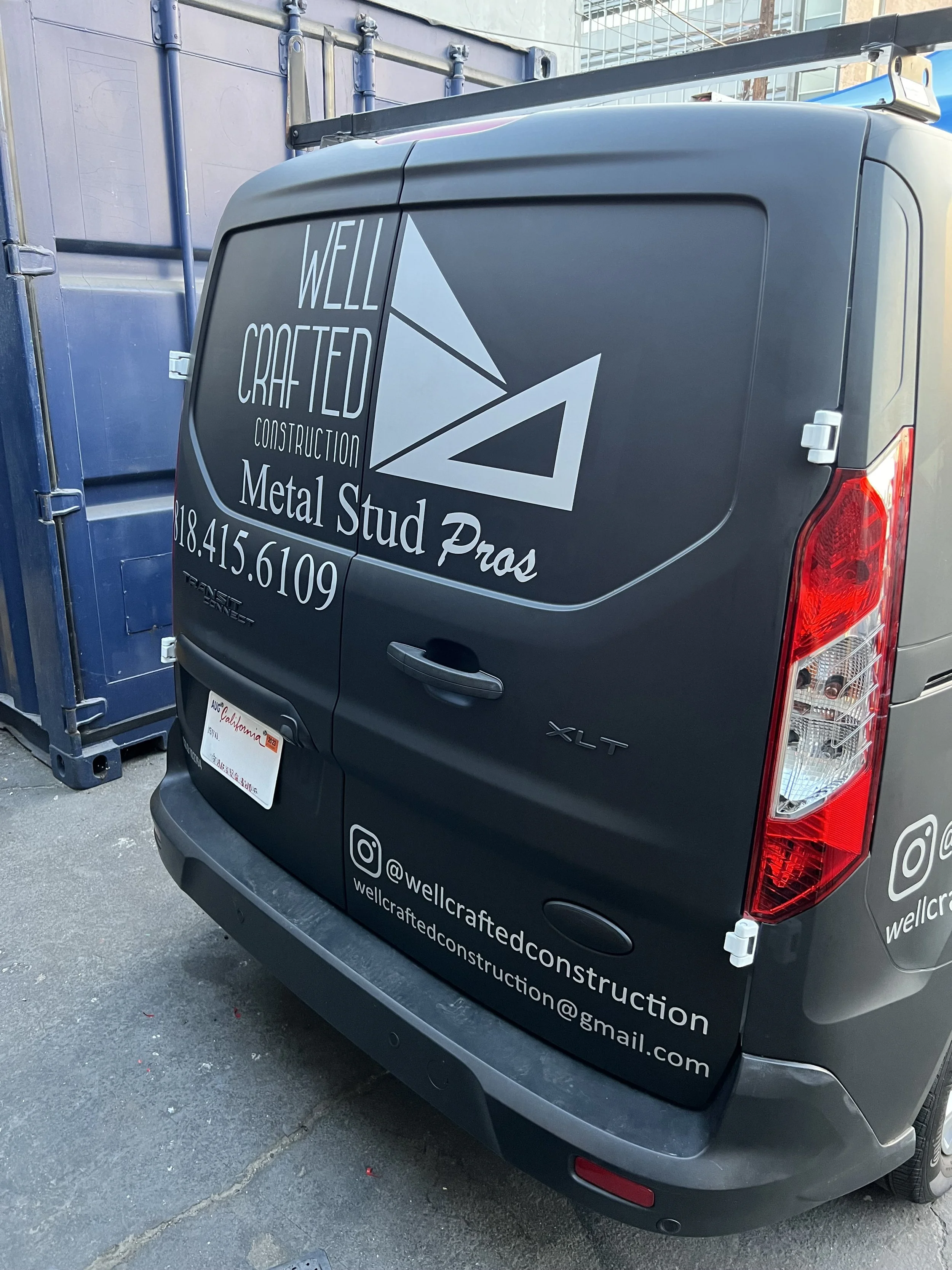 Black van with business logo and contact information for Well Crafted Construction, specializing in metal stud work, parked next to blue dumpsters. | Grizzly Signs | Los Angeles, CA | Custom Wraps