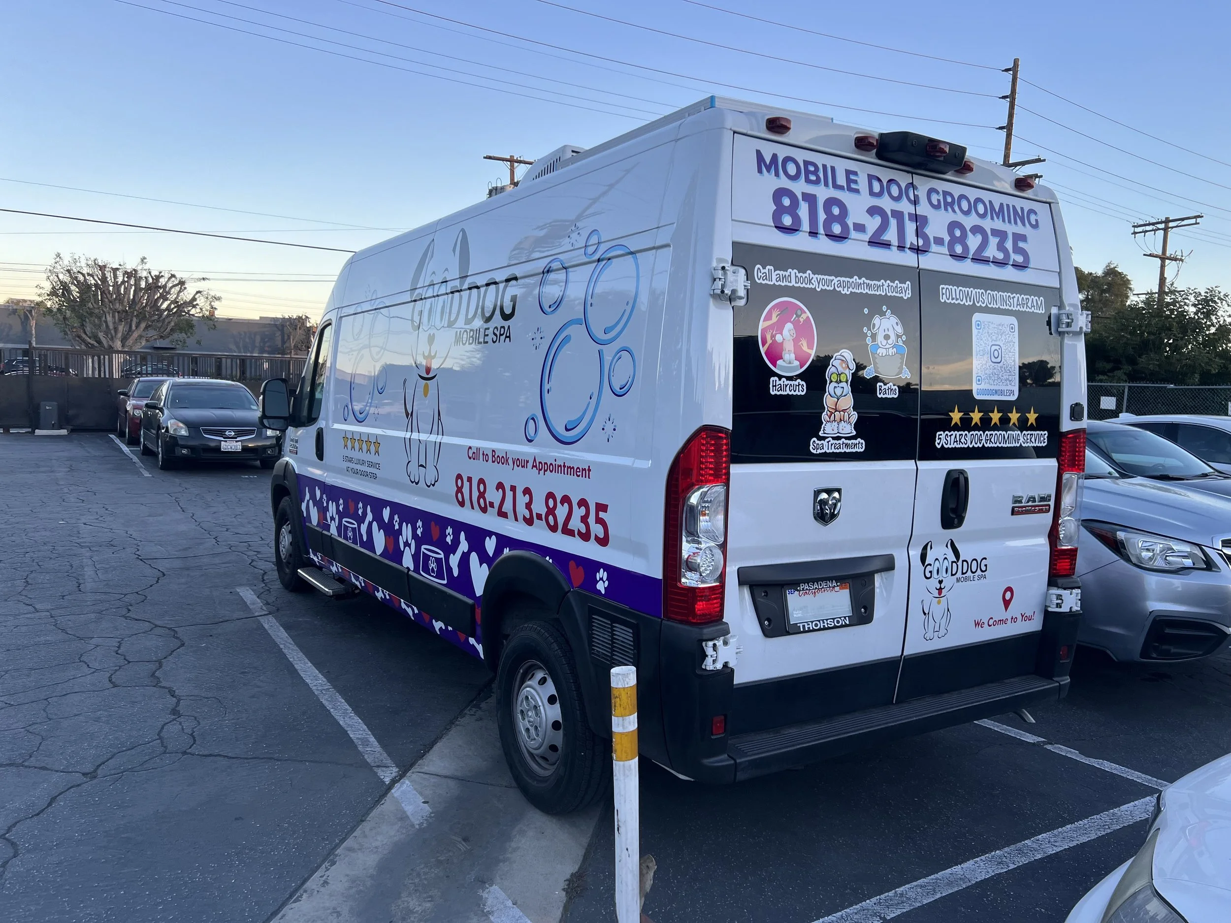 White pet grooming van with colorful graphics and text, parked in a lot. The van advertises mobile dog grooming services, including hairstylist, baths, | Grizzly Signs | Los Angeles, CA | Custom Wraps