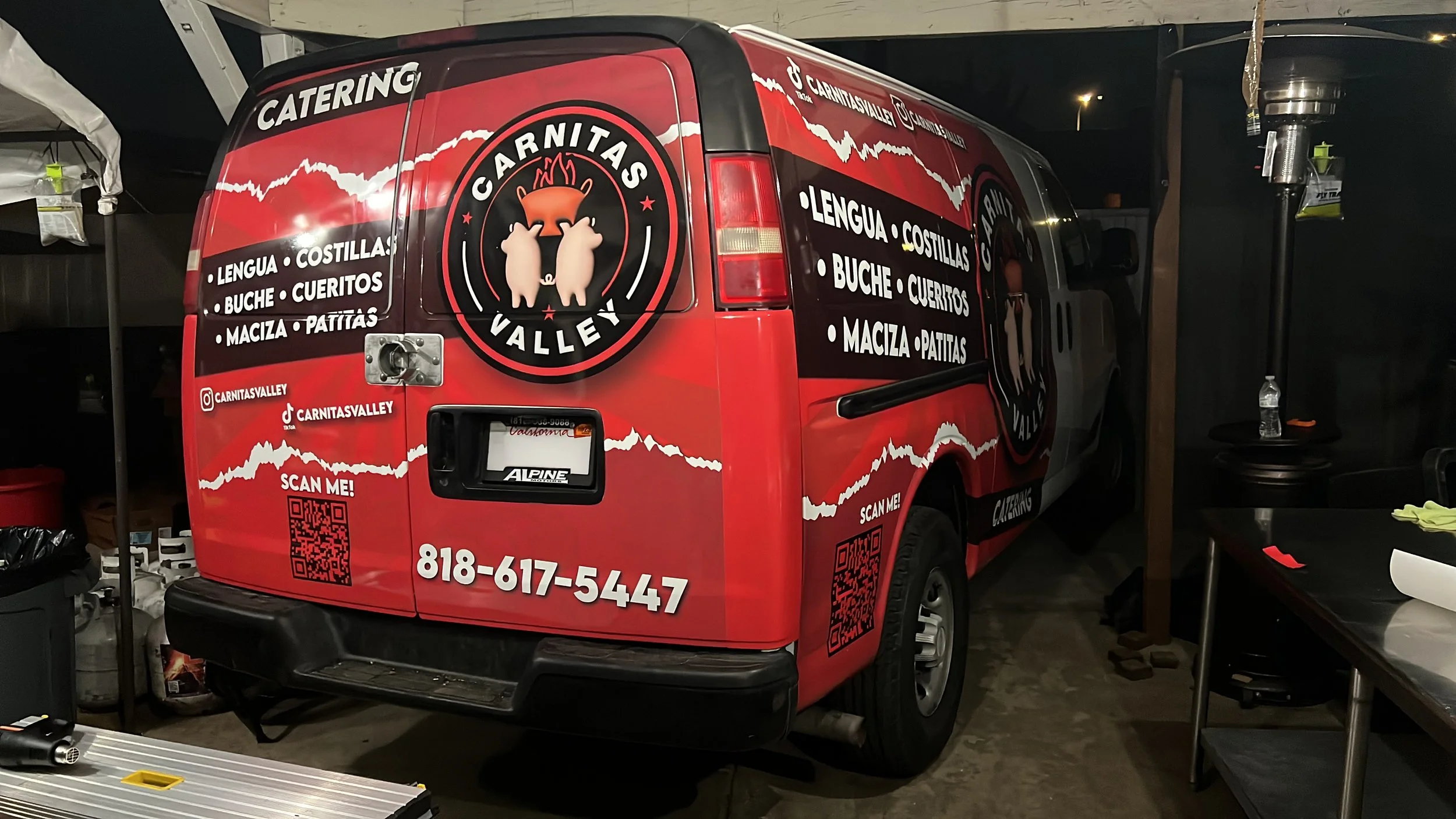 Red catering van with 'Carnitas Valley' logo and list of menu items in Spanish, parked indoors at night | Grizzly Signs | Los Angeles, CA | Custom Wraps