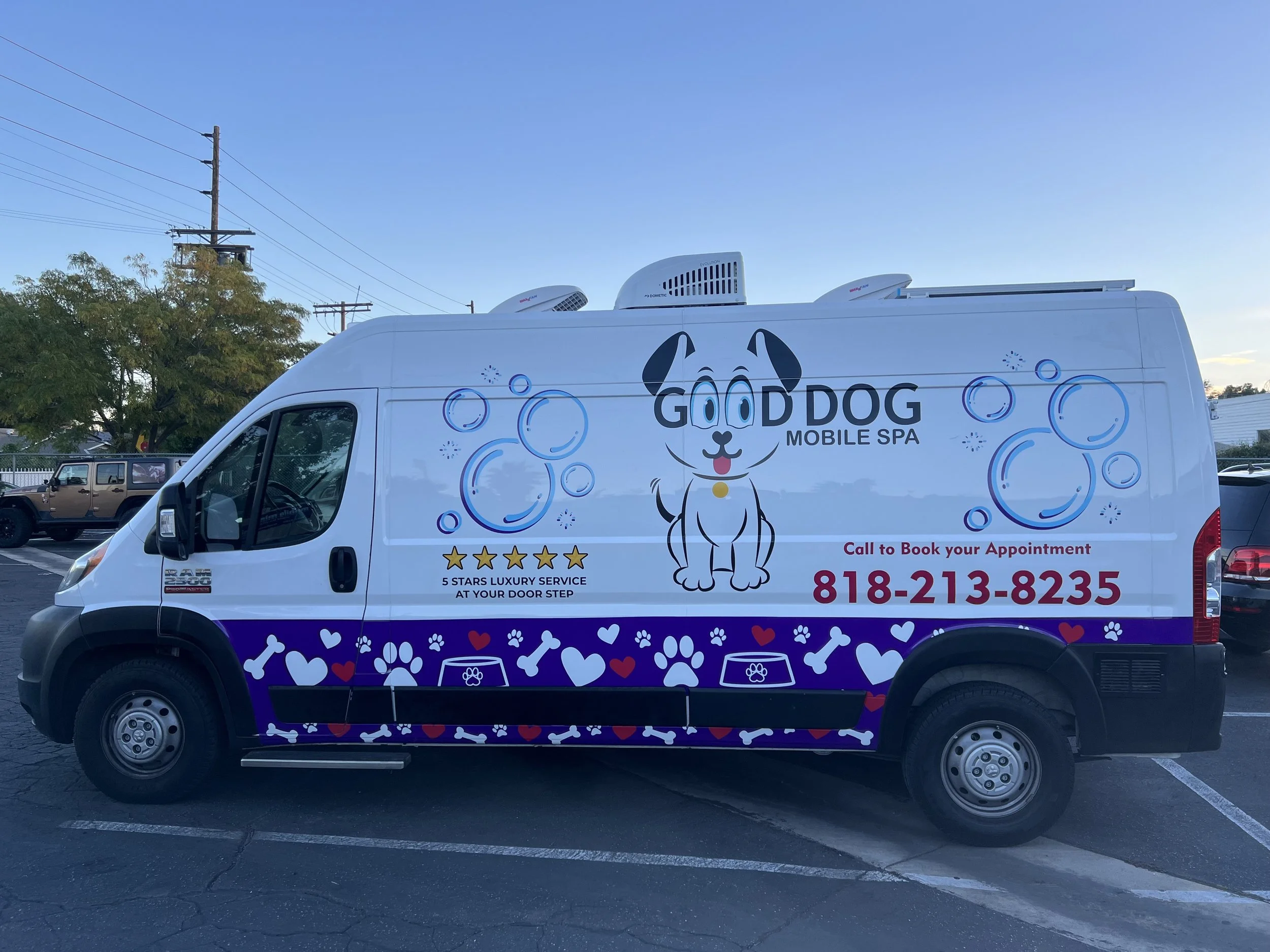 A white mobile pet grooming van with a cartoon dog, blue bubbles, paw prints, bone shapes, and a purple stripe with hearts, bones, and paw prints logo for Good Dog Mobile Spa. | Grizzly Signs | Los Angeles, CA | Custom Wraps