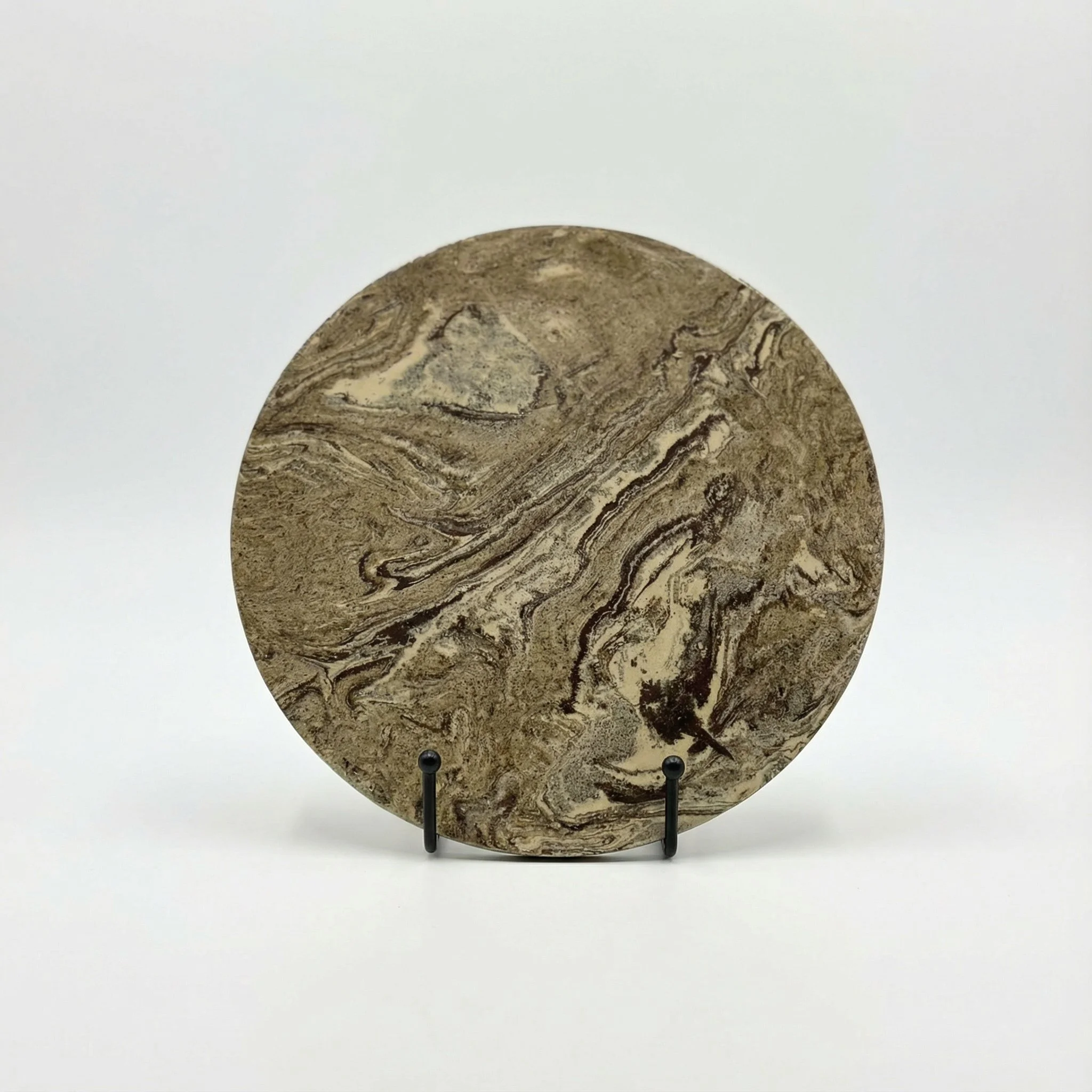 Piattello rotondo con venature marroni e beige, esposto su supporto nero