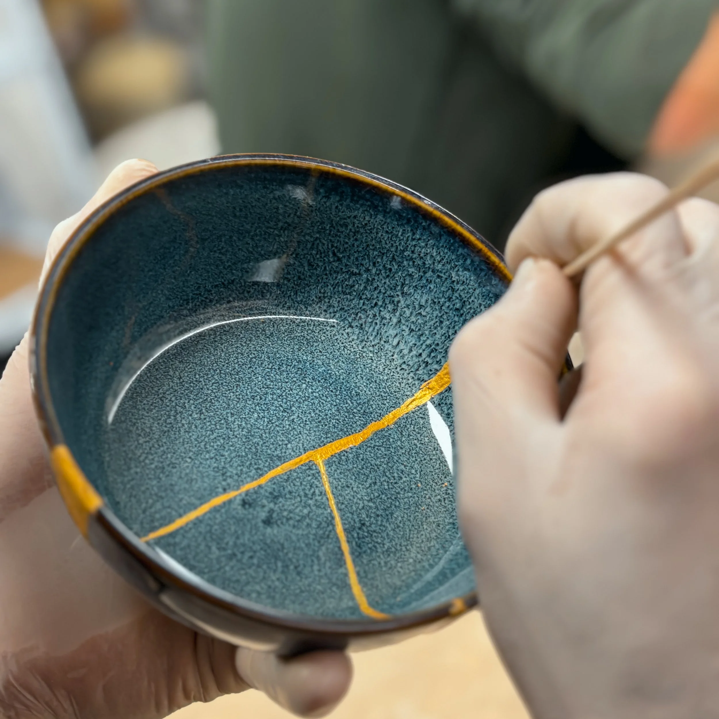 Una persona che usa uno stecchino per dipingere una linea gialla su una ciotola di ceramica blu