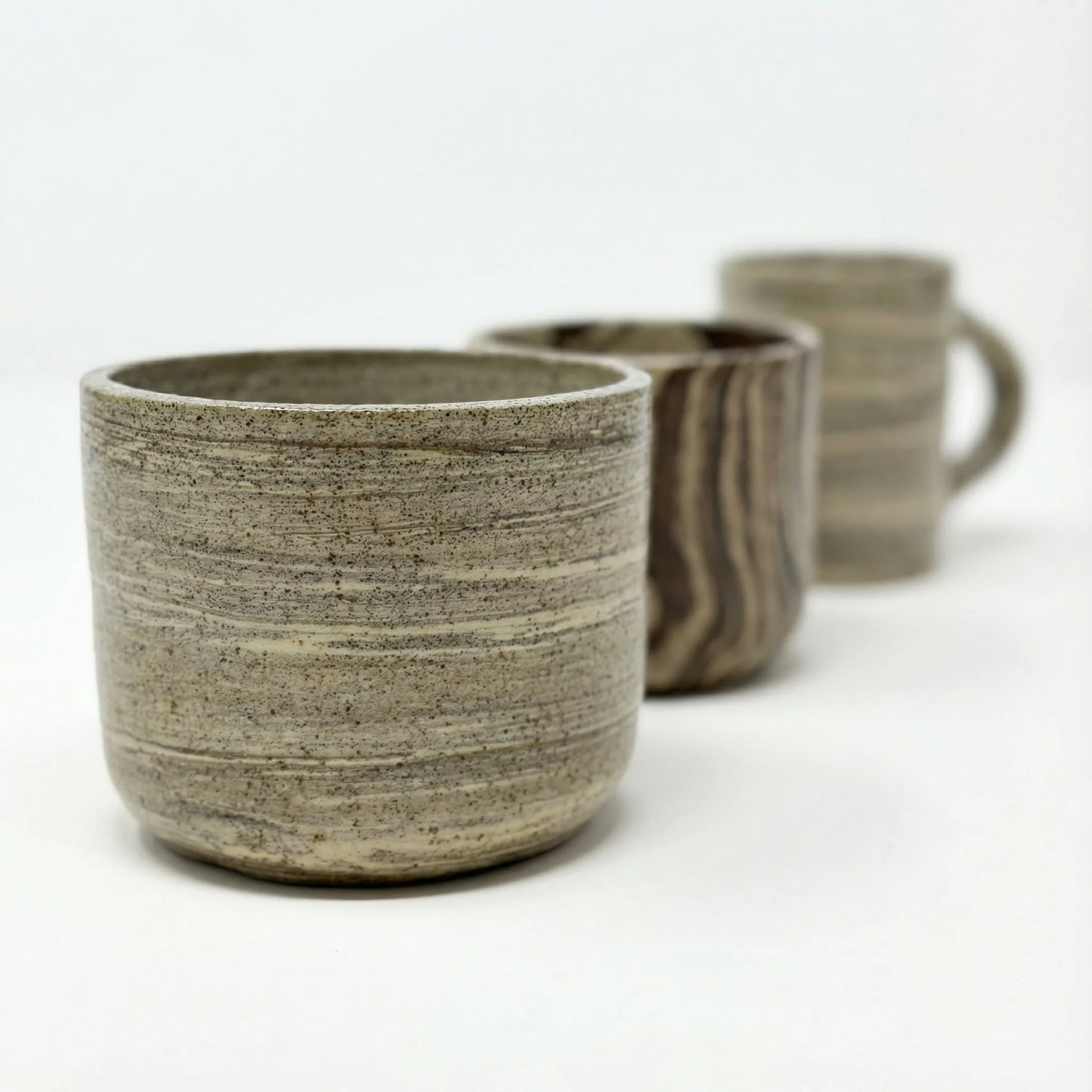 Tre tazze di ceramica con motivi naturali, ciascuna con colori e texture diverse, disposte in fila su uno sfondo bianco.