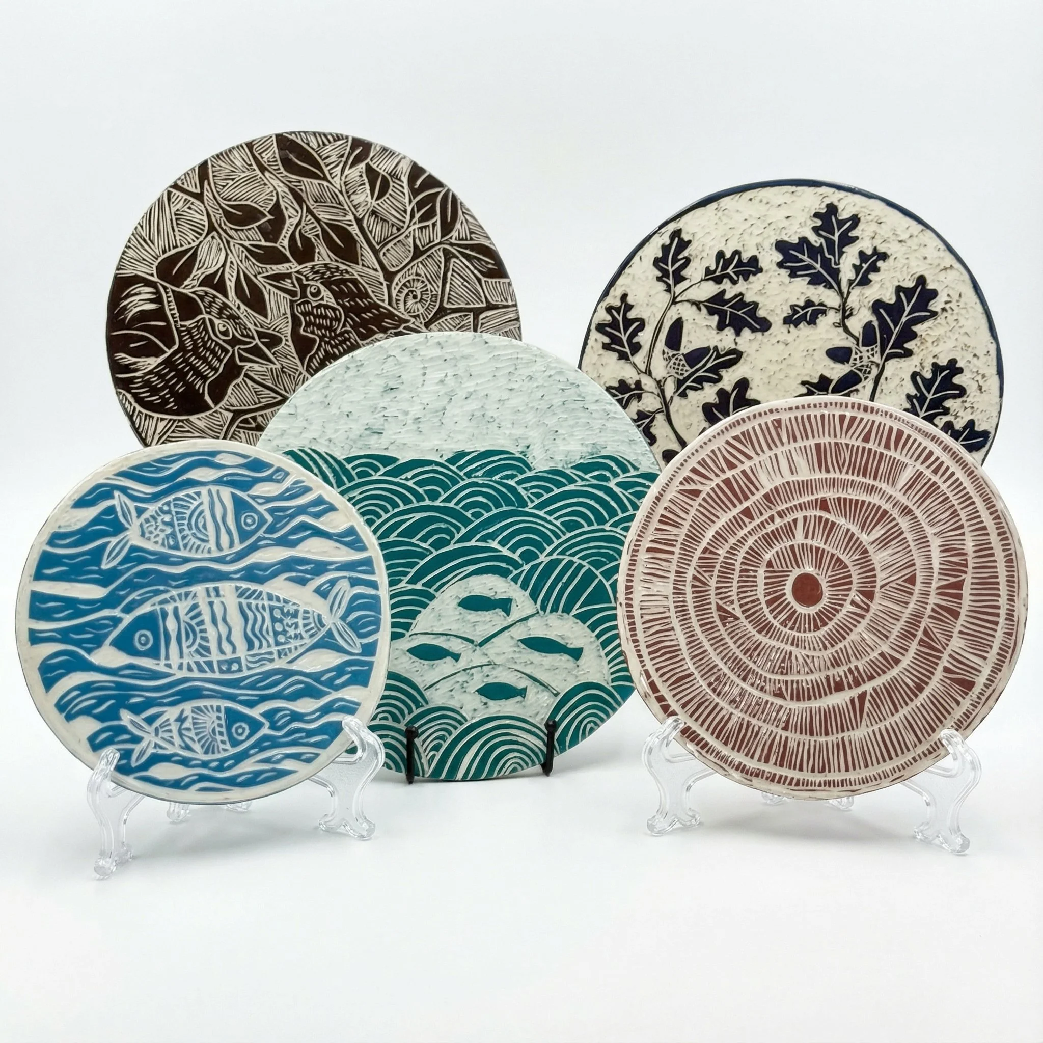 Set di piatti decorativi con motivi di animali, piante e onde, disposti su supporti di plastica trasparente.