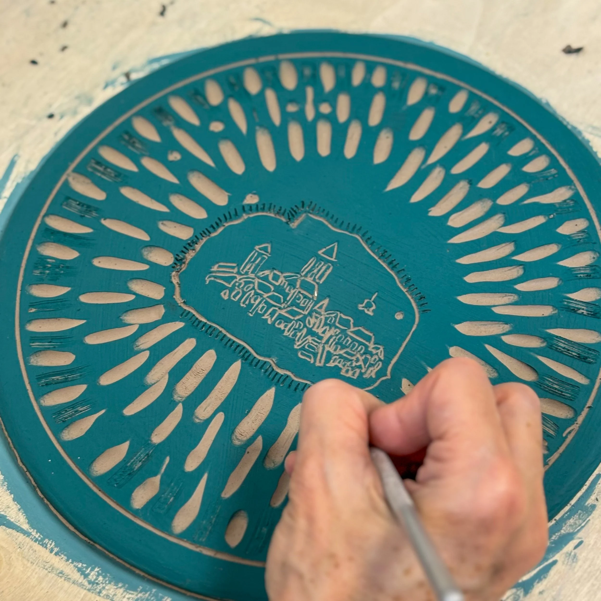 Una persona sta incidendo una targa in metallo con un'incisione di una mappa di un'isola con edifici e barche.