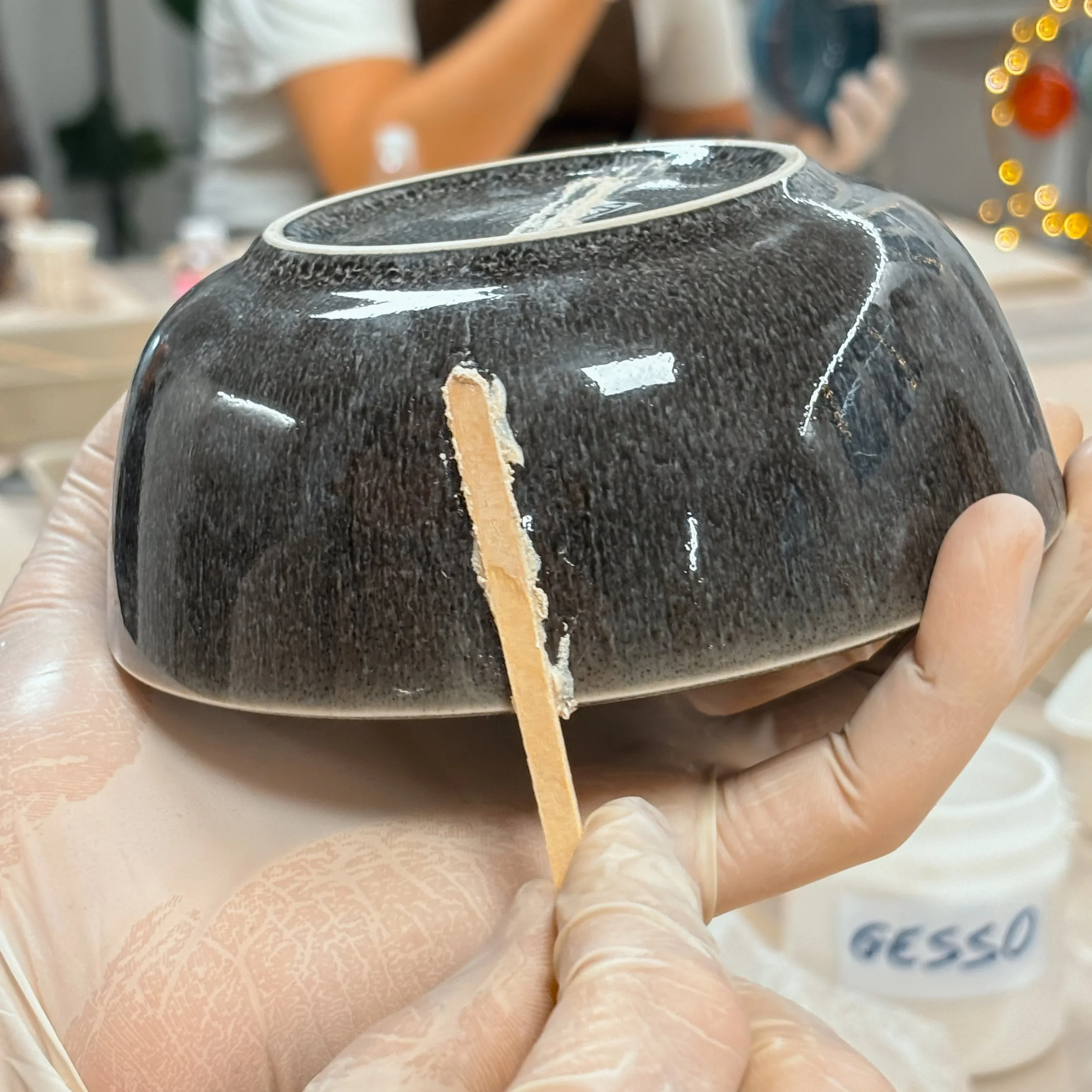 Una persona indossa guanti intorno a un oggetto di ceramica nera e lucida, durante un processo di lavorazione oppure di conservazione.