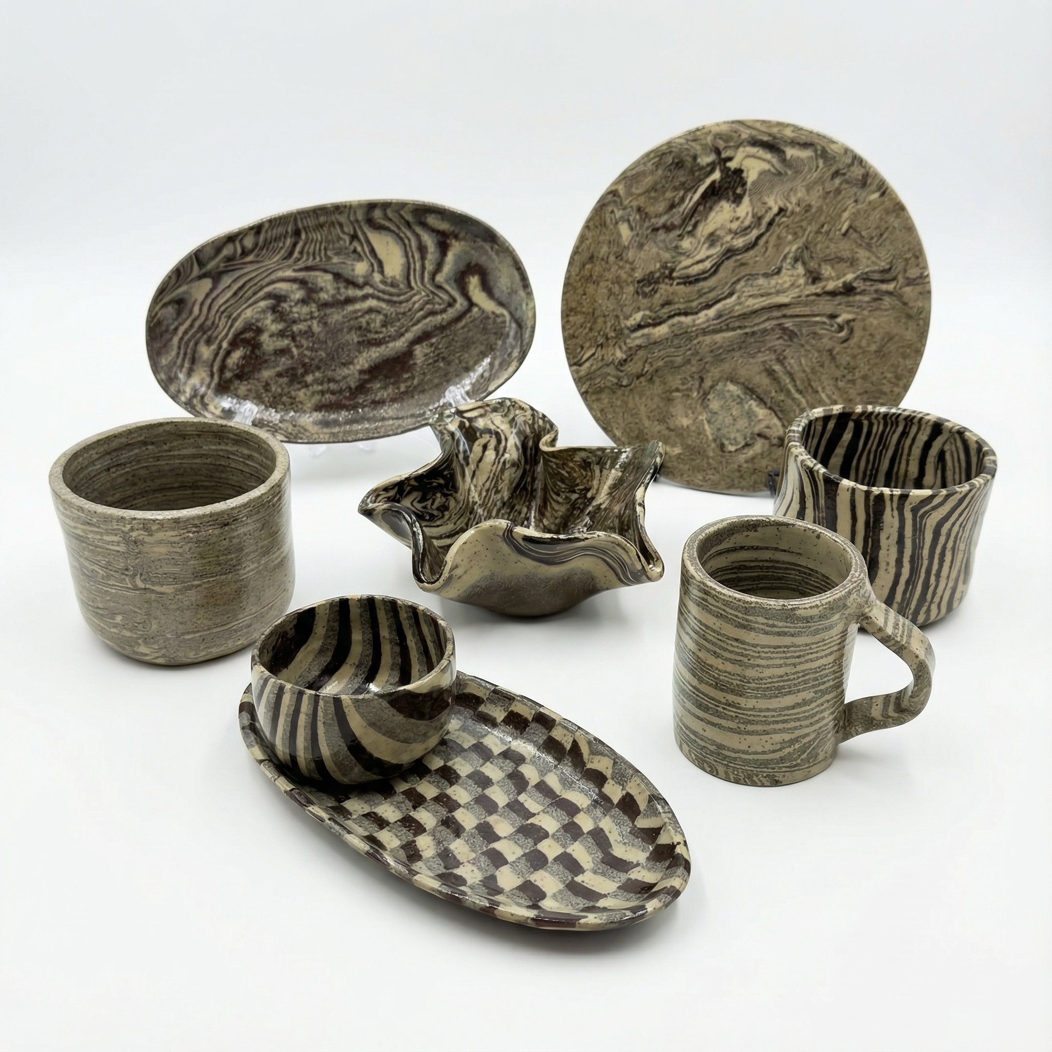 Set di ceramiche in ceramica con motivi a strisce e marmorizzati, tra cui ciotole, tazze, un piatto ovale e un vaso decorativo.