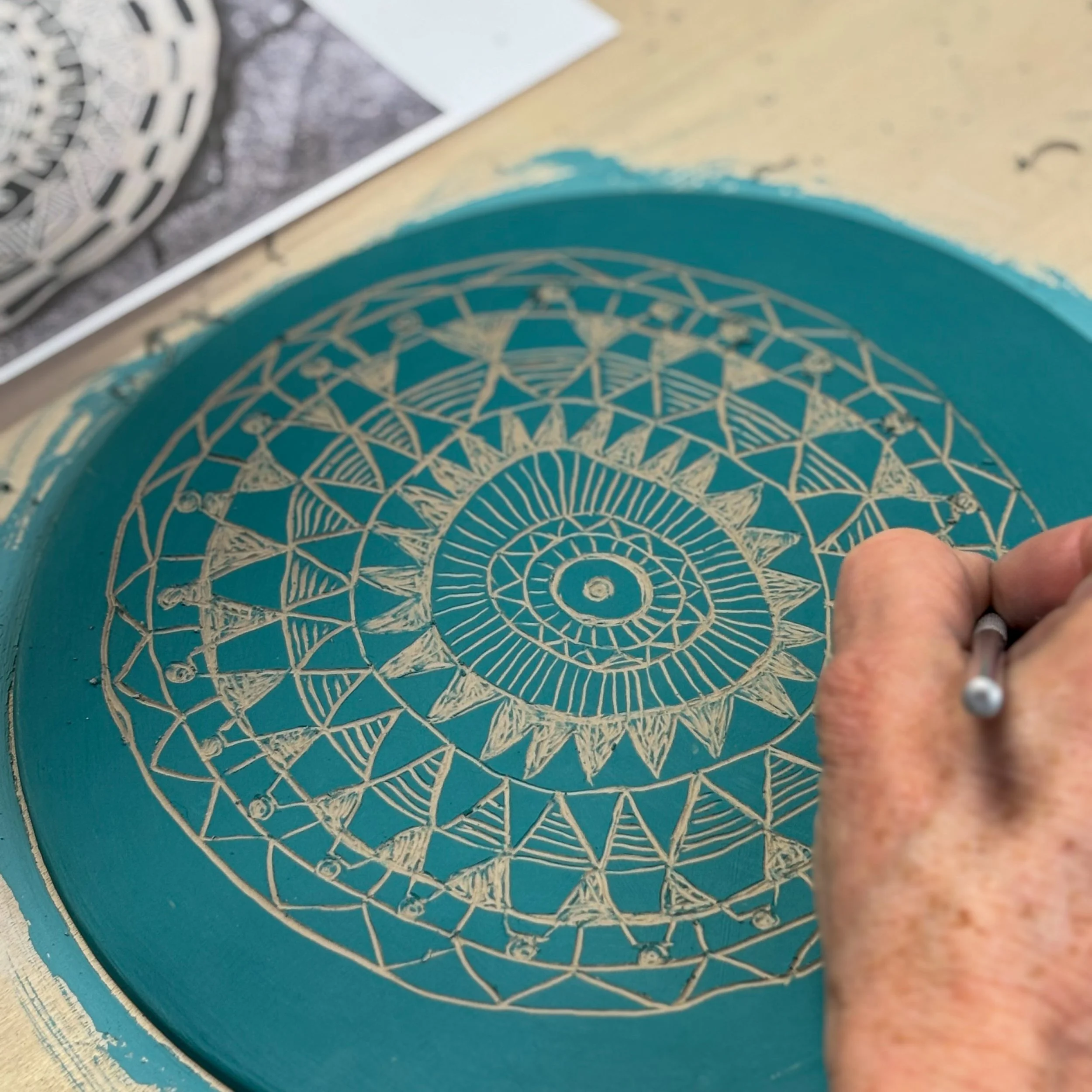 Una mano disegna un mandala complesso su una superficie circolare blu, con strumenti di disegno visibili.