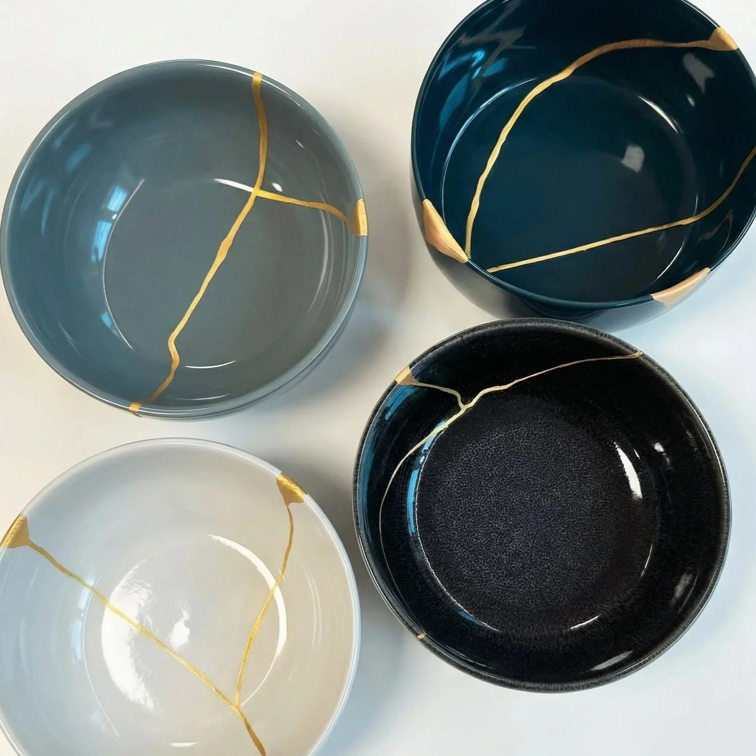 Quattro ciotole di diversi colori e materiali con decorazioni in oro, disposte su una superficie bianca.