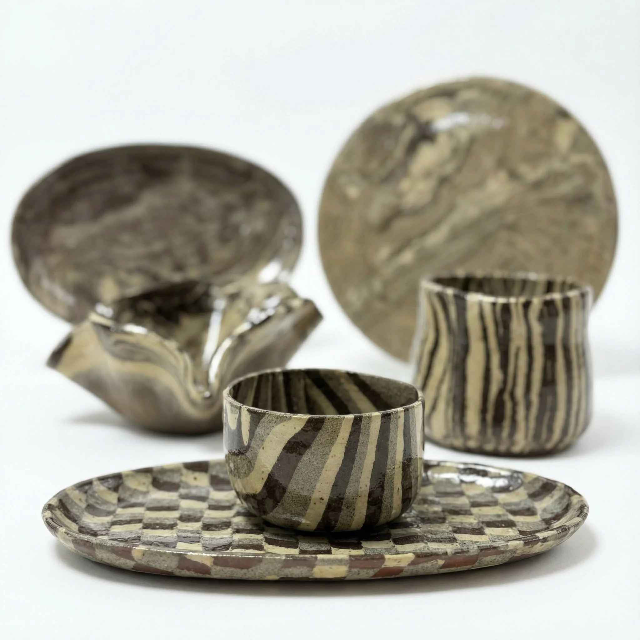 Set di ceramiche artistiche con motivi geometrici in tonalità di marrone e beige, include una ciotola, un piatto, due coppe e piattino.