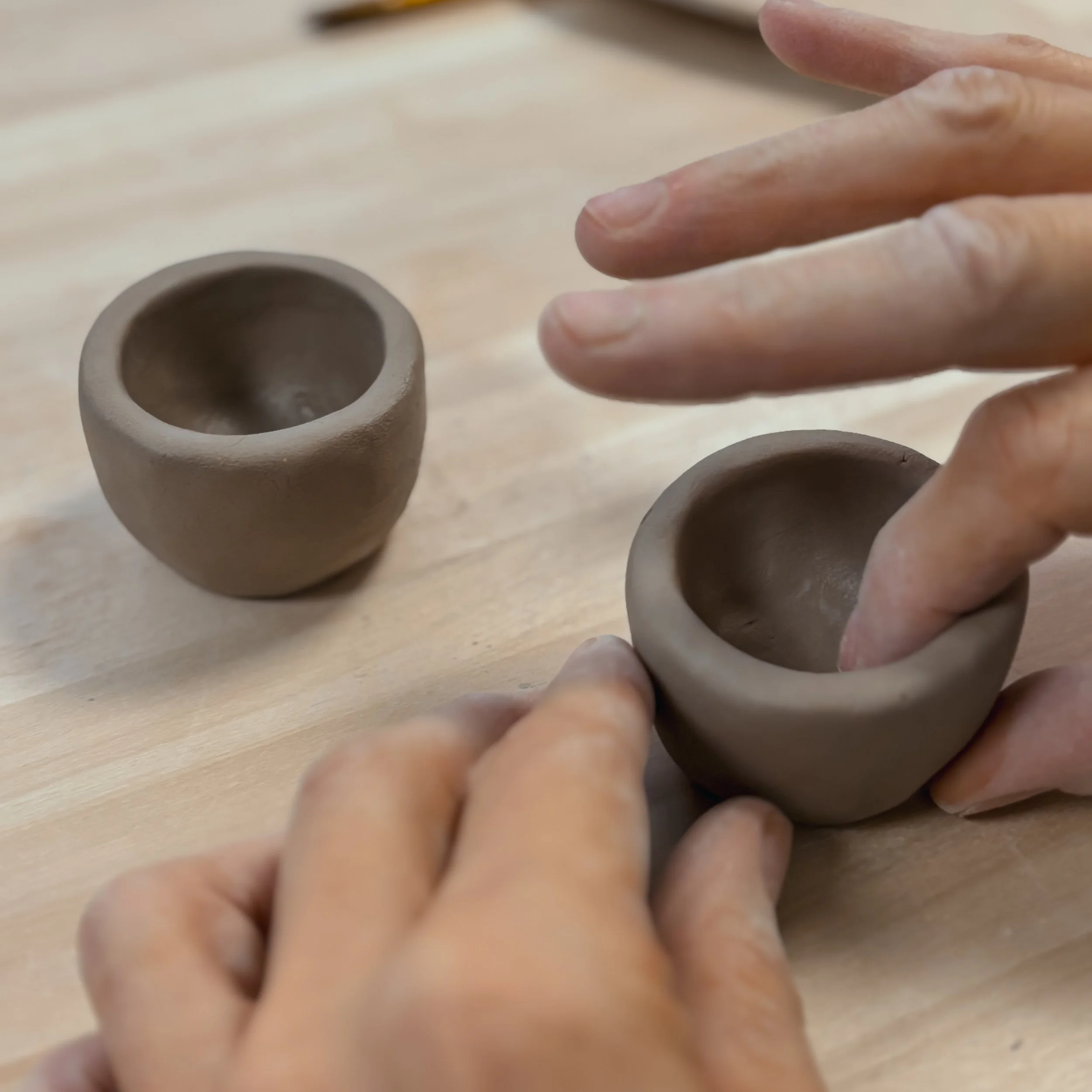 Mani che modellano due piccole ciotole di argilla su un tavolo di legno.