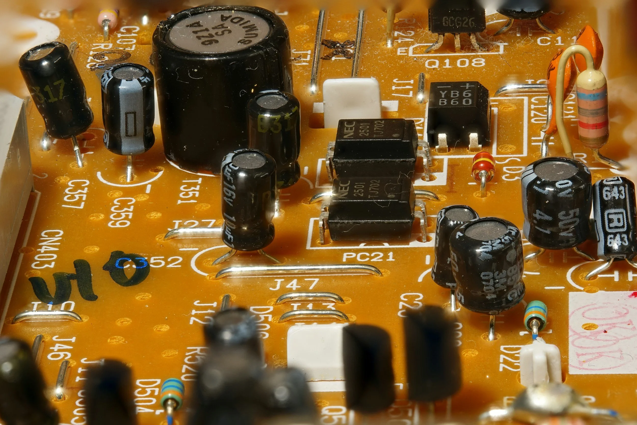 Close-up photo of a yellow printed circuit board (PCB) with various electronic components including capacitors, resistors, and integrated circuits.