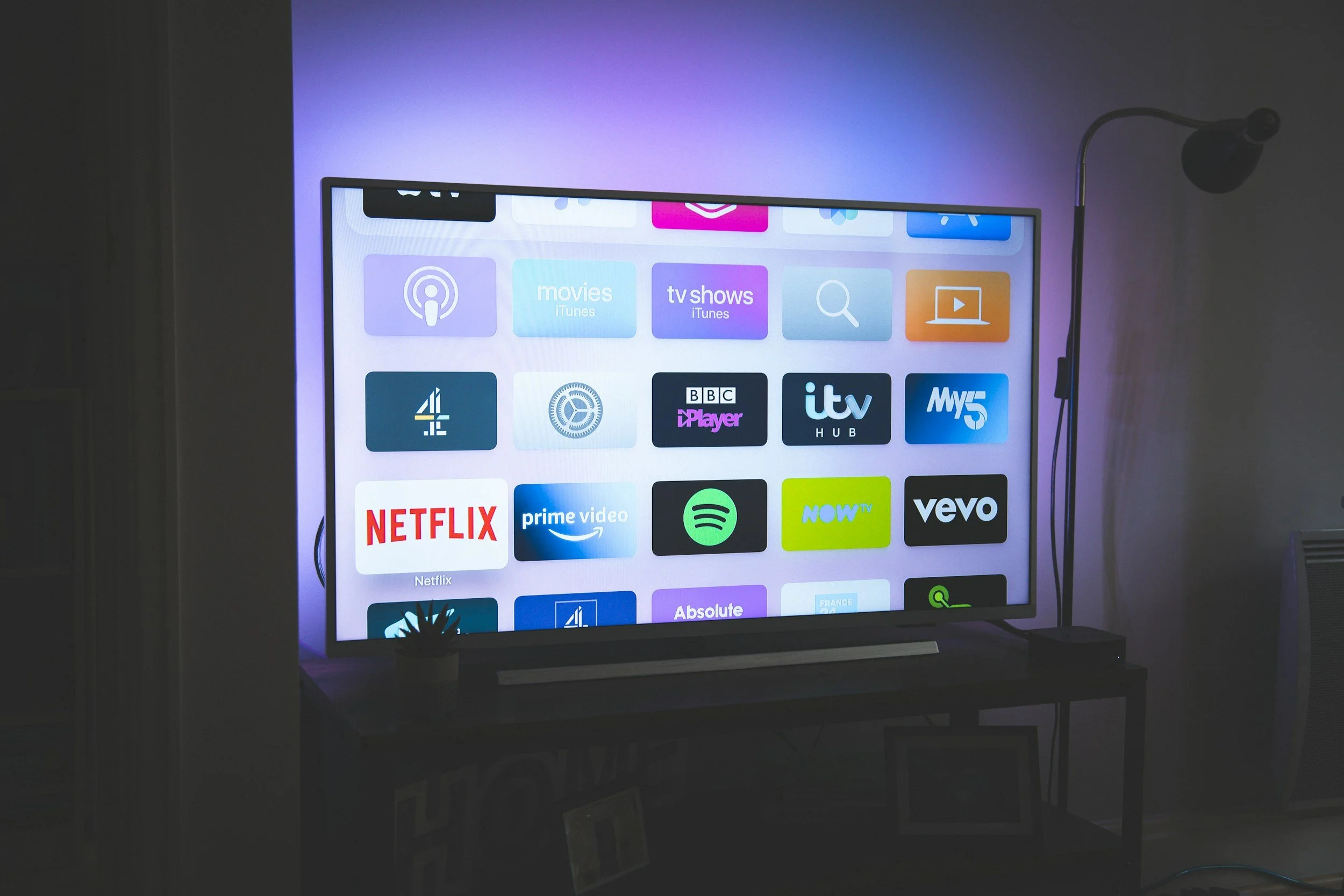 Smart TV screen displaying various streaming service app icons, including Netflix, YouTube, Spotify, and BBC iPlayer, in a living room setting.