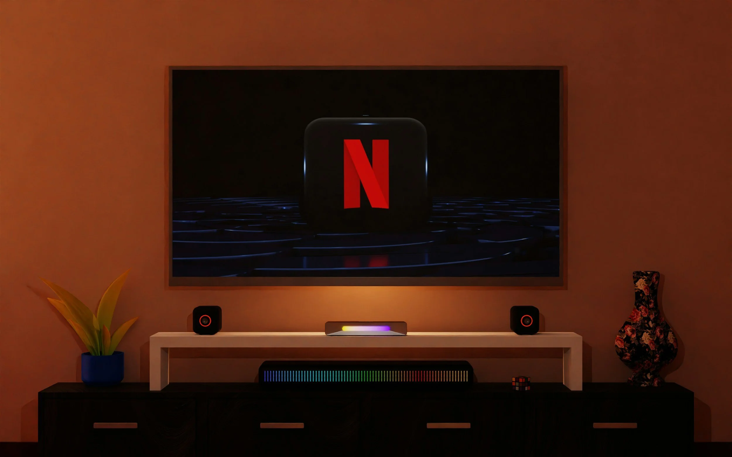 A modern living room setup with a wall-mounted TV displaying the Netflix logo on a black background. Below the TV is a white console with two small black speakers, a colorful equalizer, and a central device with a rainbow-colored light. To the left of the console is a blue pot with a yellow-green plant, and to the right is a floral vase. A small Rubik's cube is on the right side of the console.