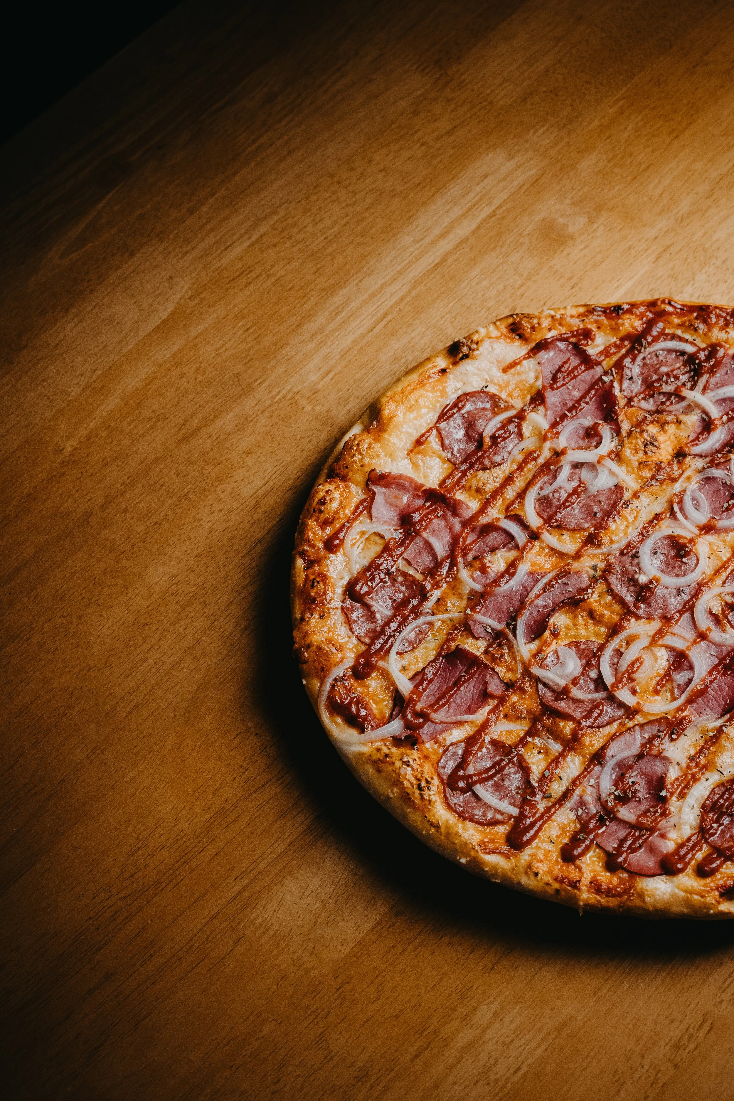 A half pizza with ham and onions on a wooden table.