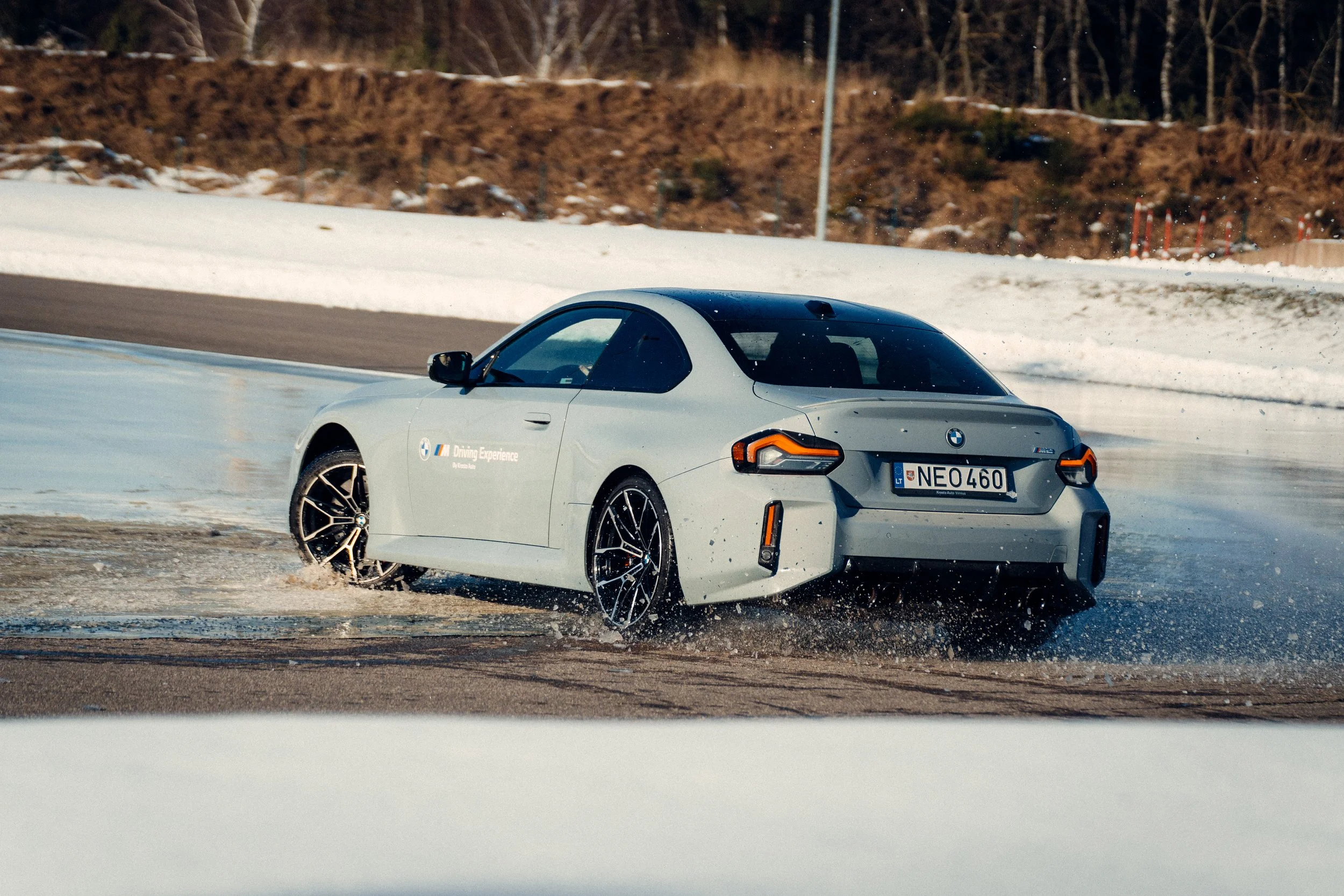 A white BMW M Series car driving on a snowy and icy race track with snow-covered ground and trees in the background.