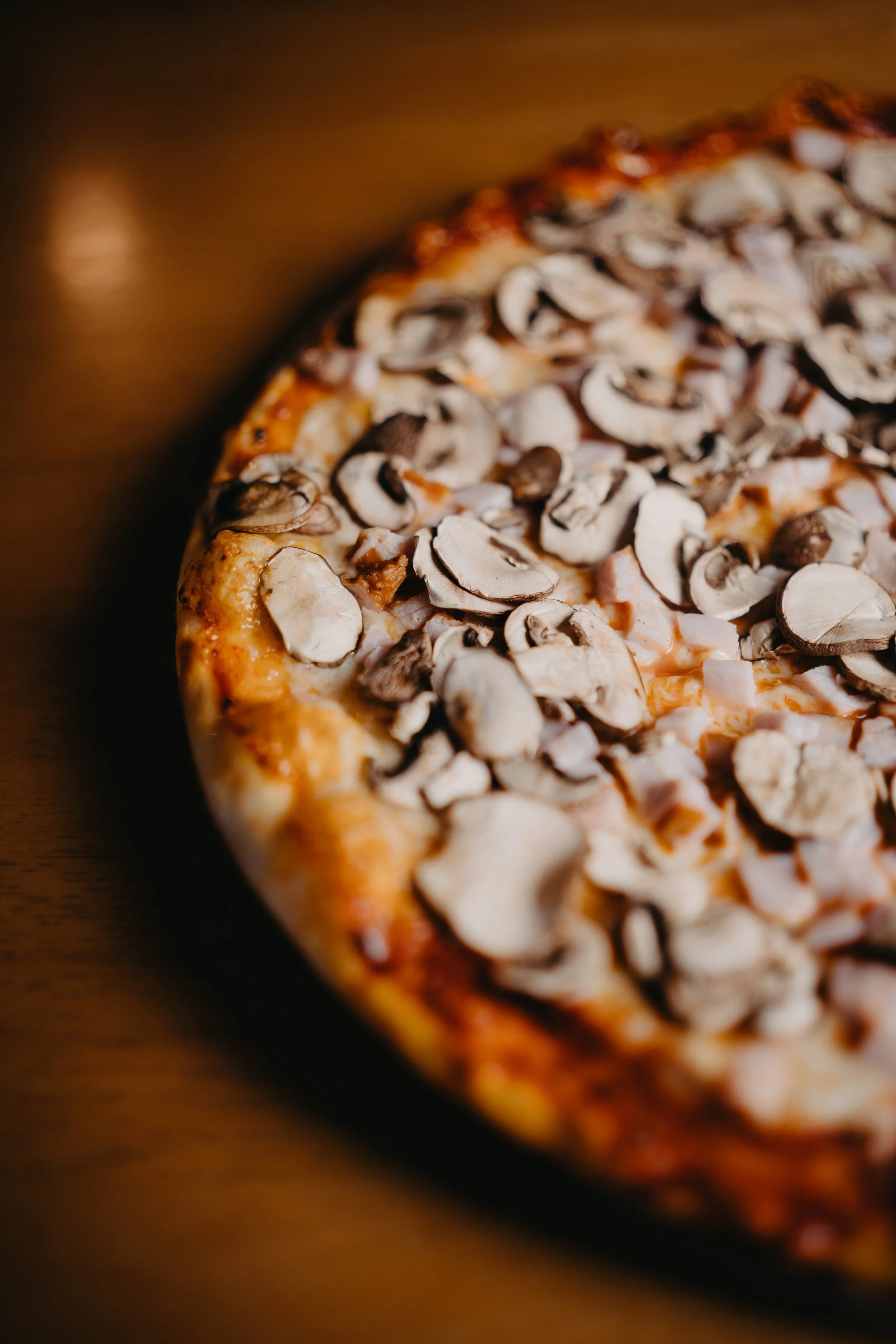Close-up of a mushroom pizza with melted cheese on a wooden surface.