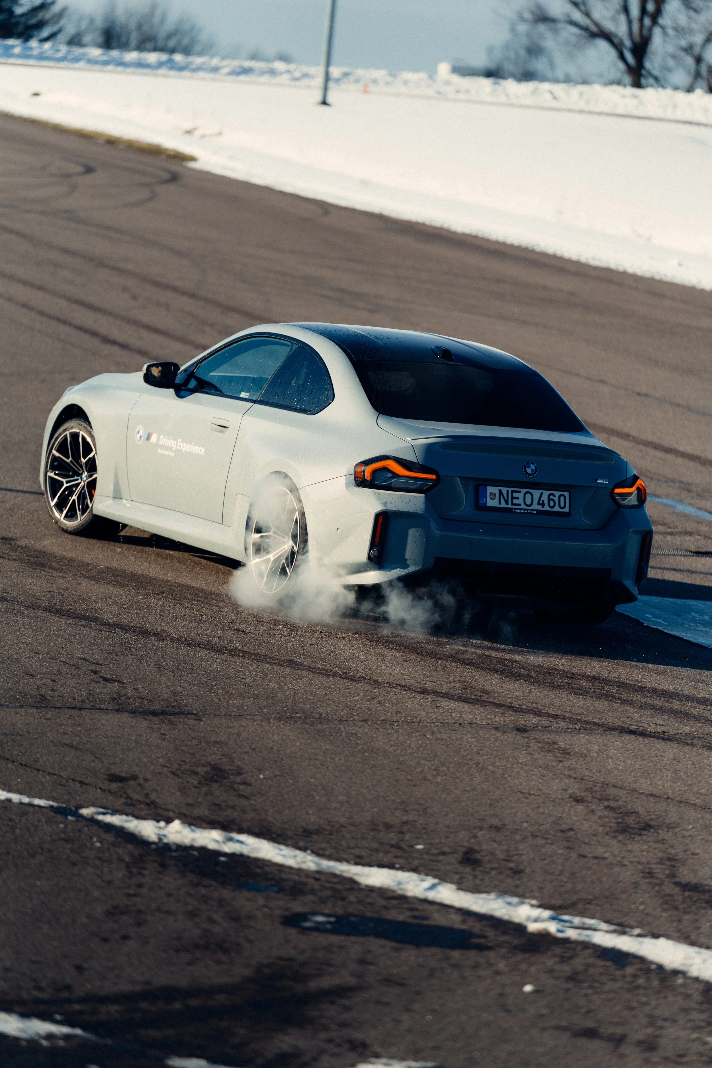 A white BMW sports car drifting on a racetrack with snow in the background, smoke coming from the rear tires.