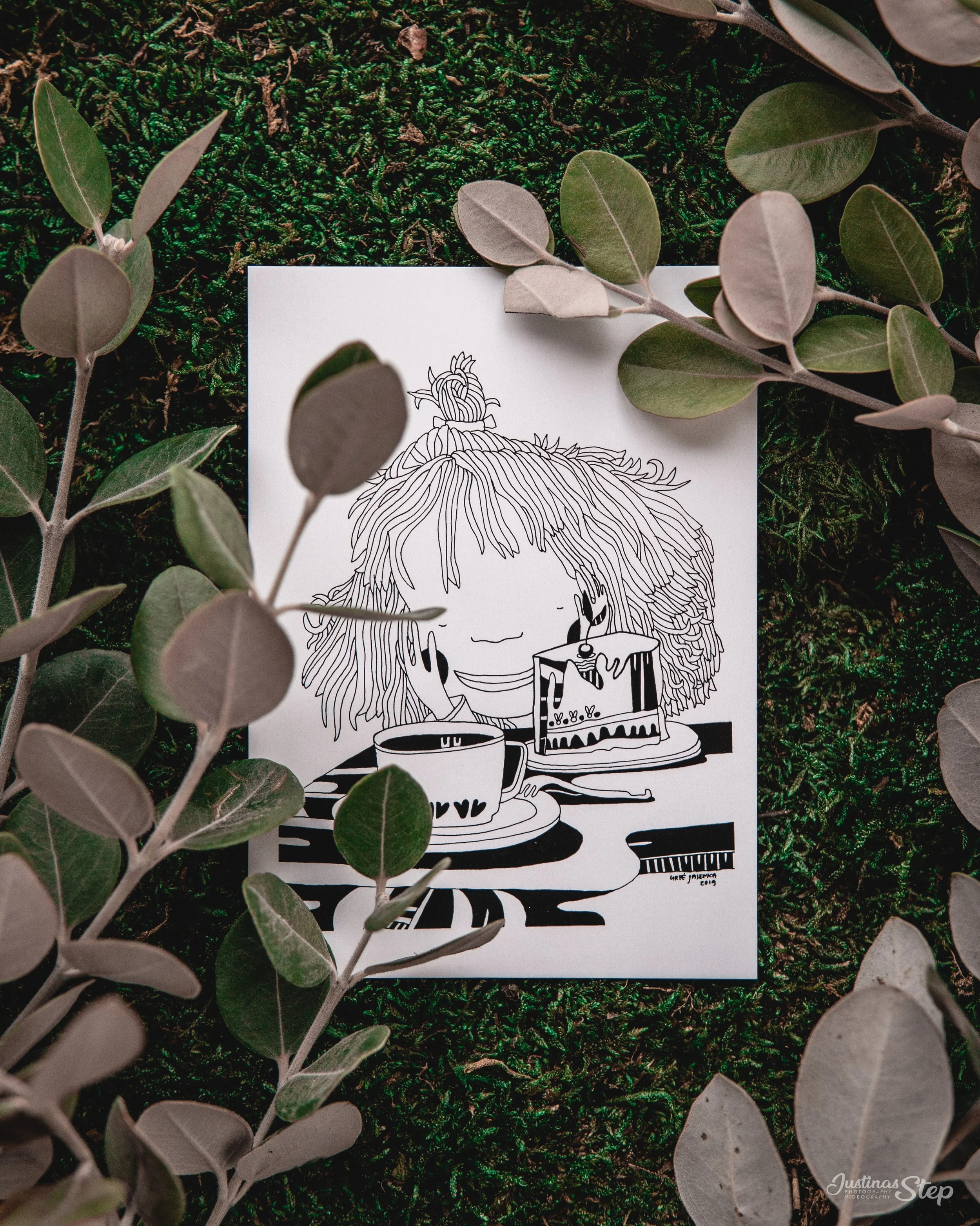 A black and white illustration of a girl with curly hair enjoying a cup of coffee and a slice of cake, surrounded by leaves on a mossy ground.