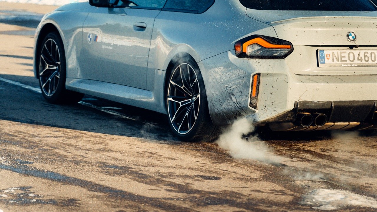 A silver BMW car kicking up smoke or steam from its exhaust pipe on a road.