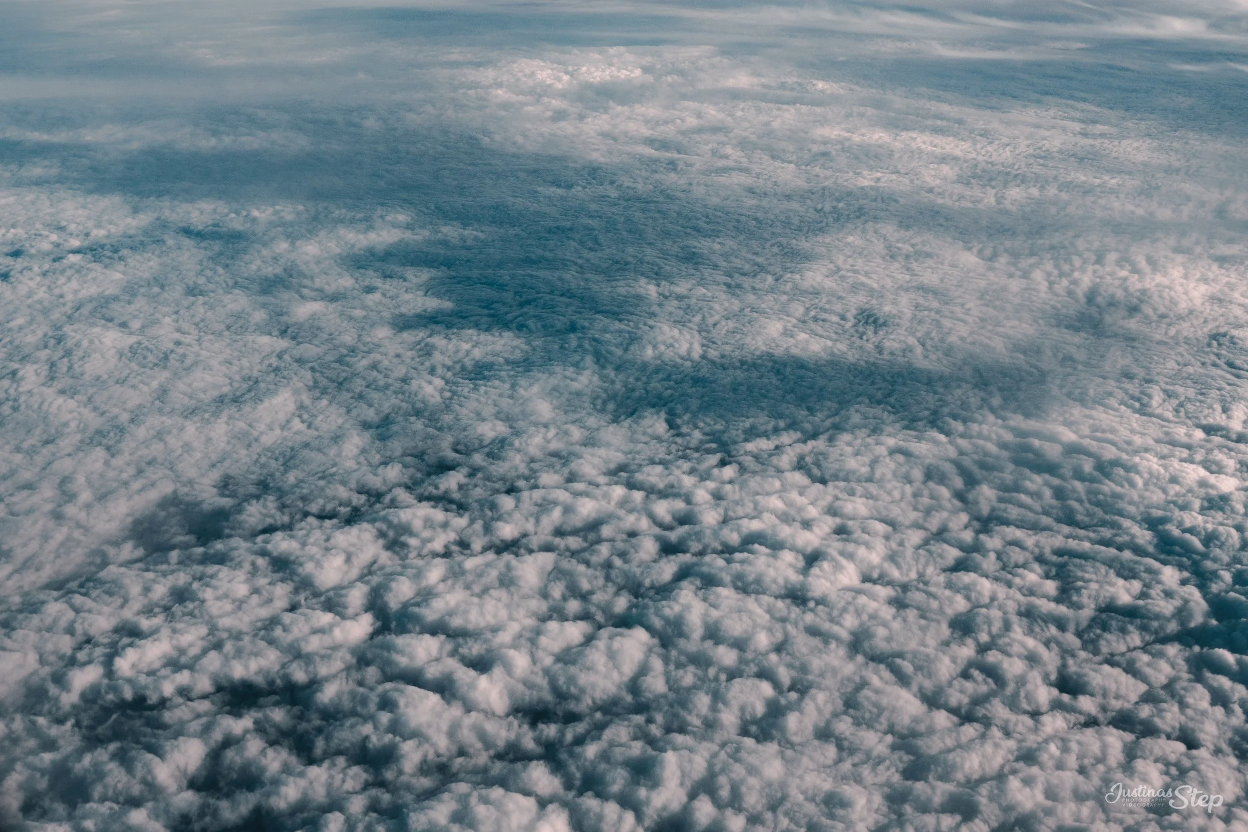 Photo taken from above the clouds showing a vast cloudscape with varying textures and shades of white and gray.