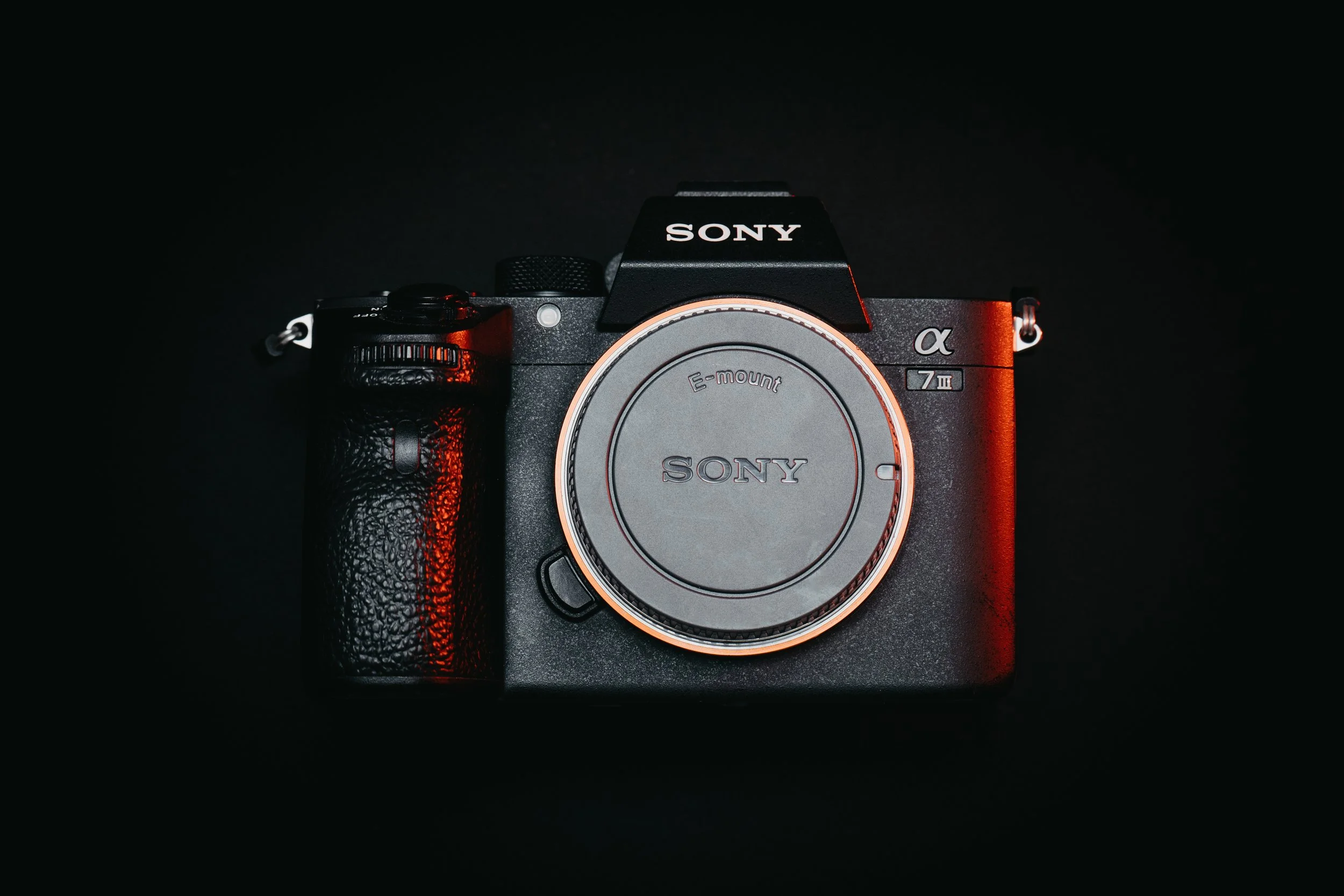 Black Sony Alpha a7 III mirrorless camera with a gray lens cap on a black background.