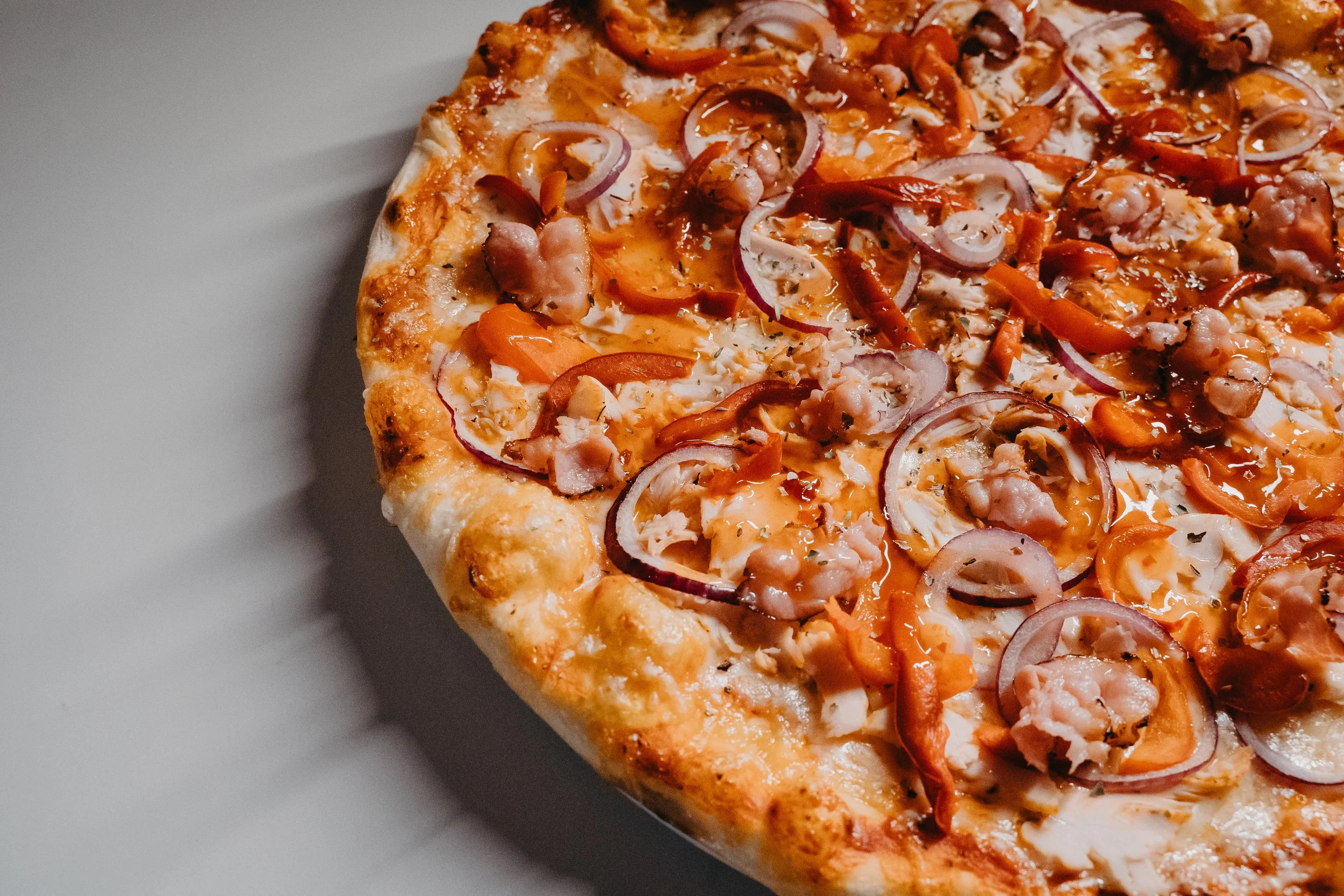 Close-up of a pizza with cheese, red onions, bell peppers, and chicken.