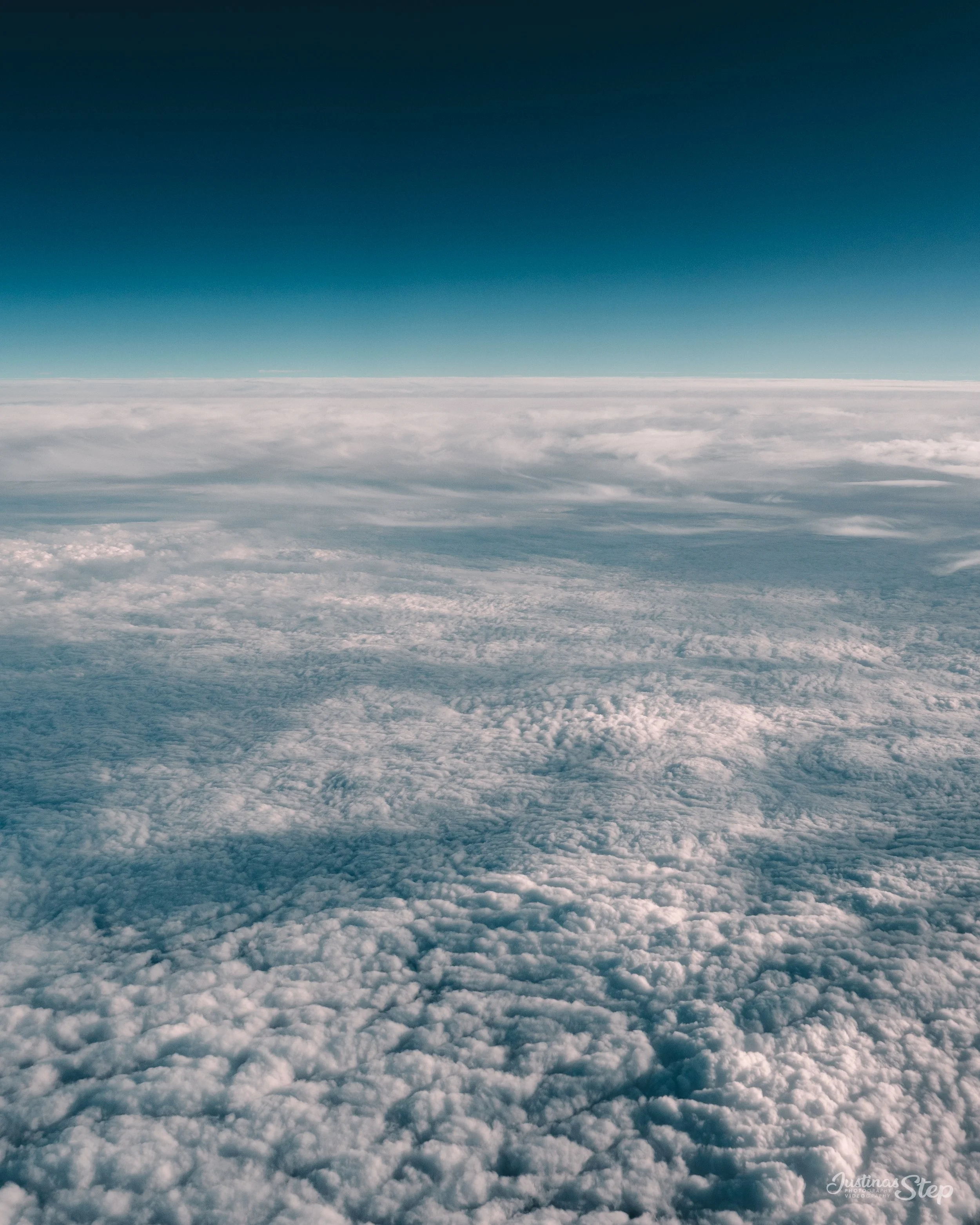 View of clouds from high above, with a clear blue sky and horizon in the distance.