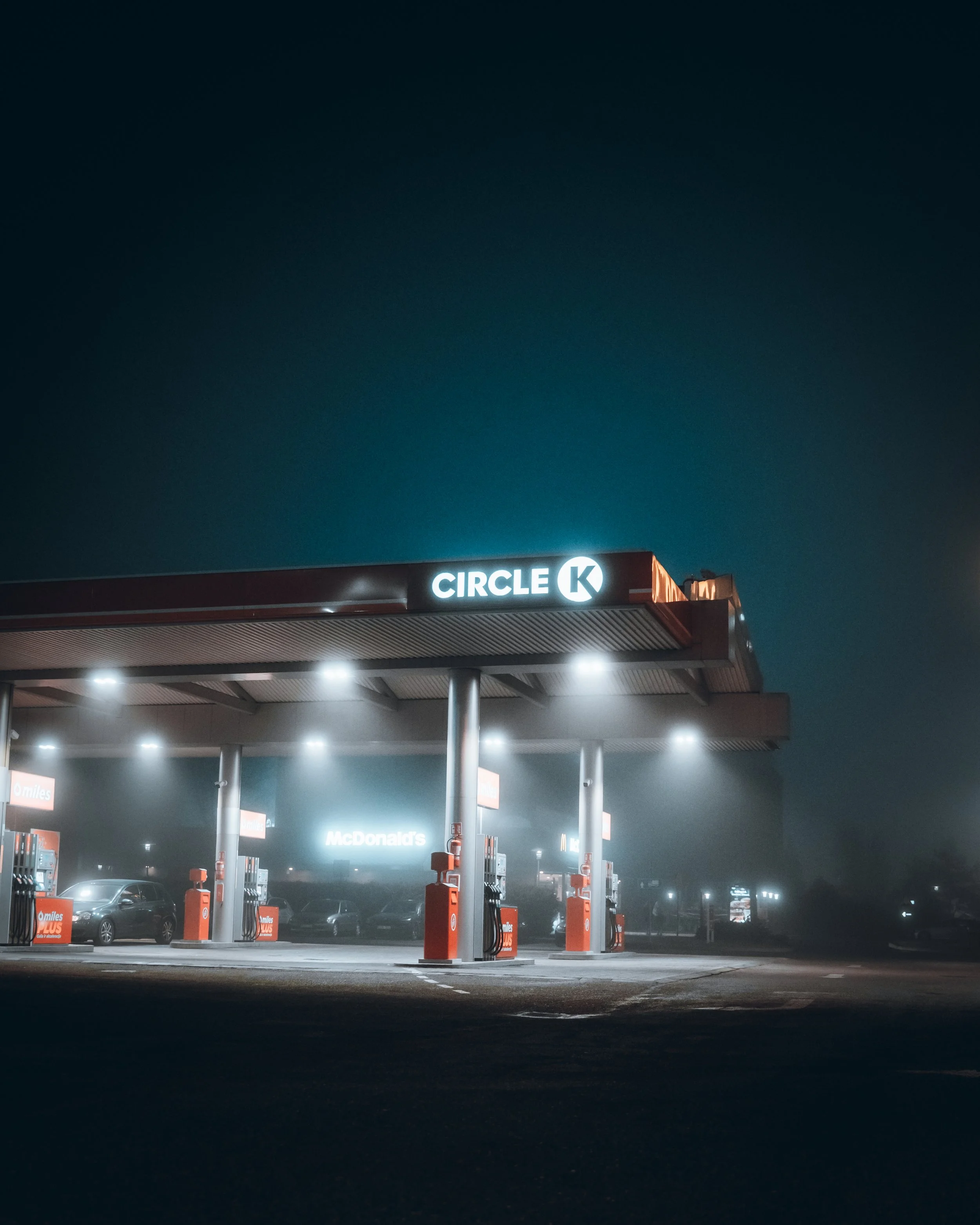 Empty Circle K gas station at night with some parked cars and a McDonald's sign in the background.