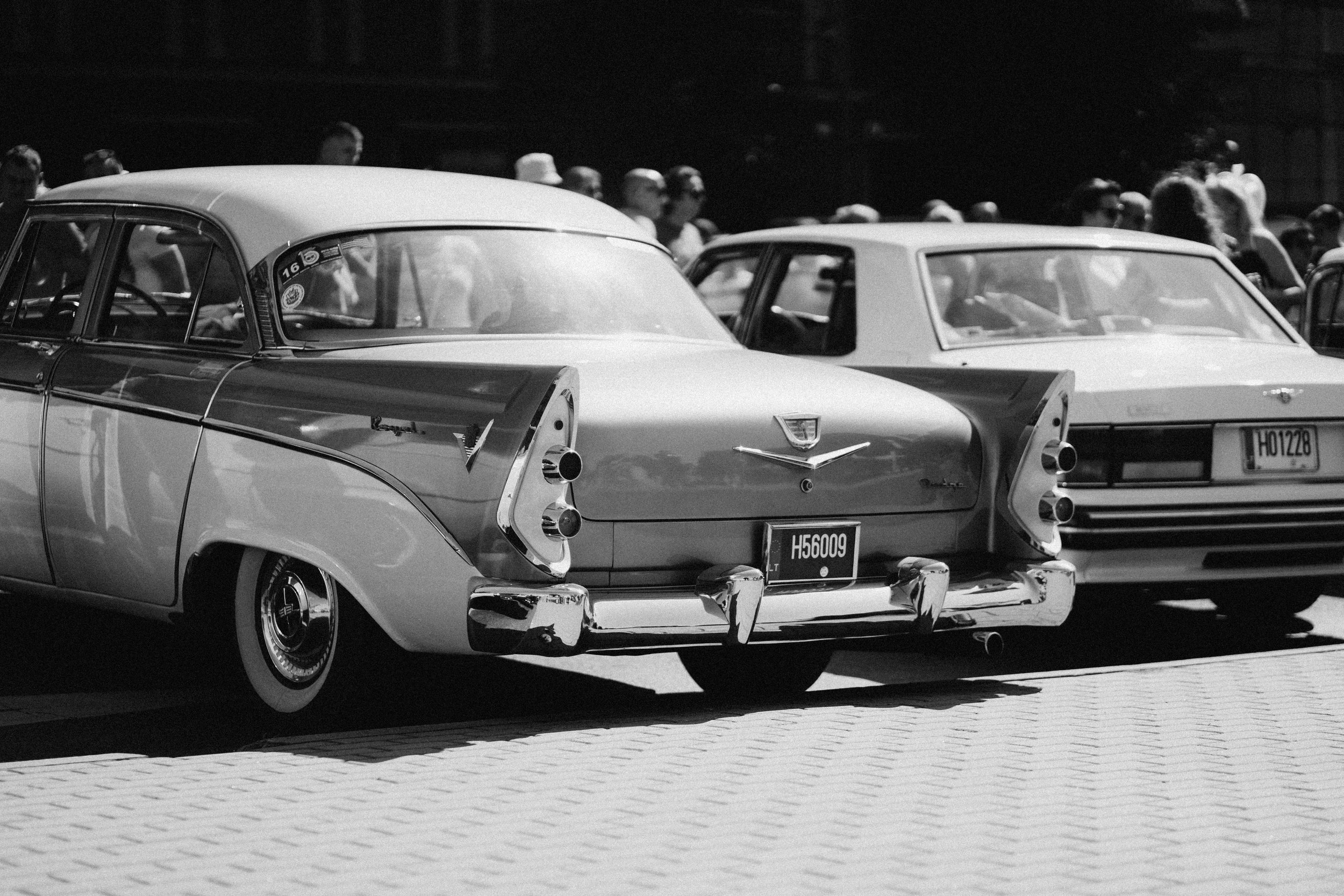 Black and white photo of two vintage cars parked side by side with people gathered in the background.