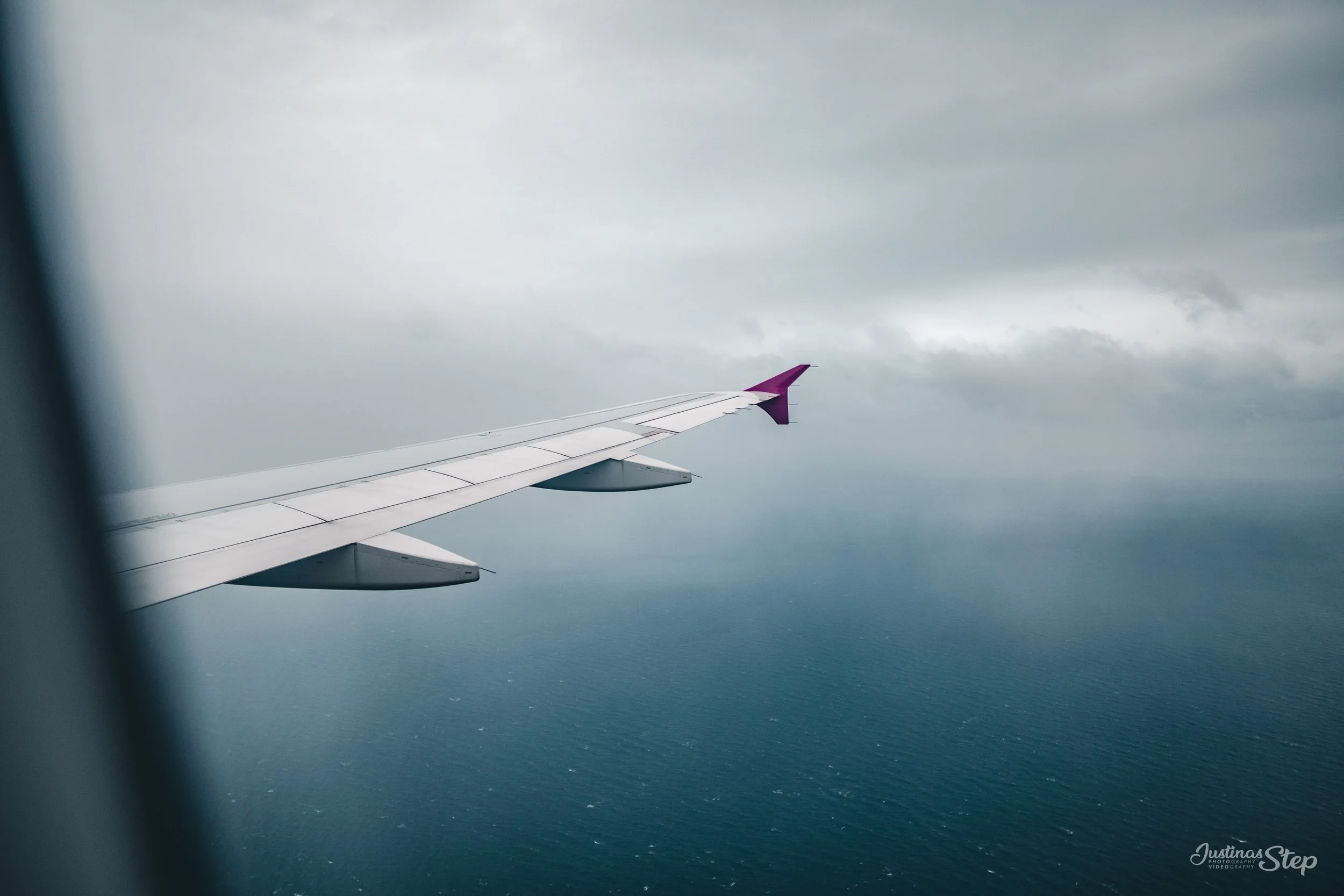 View of airplane wing over ocean with cloudy sky.