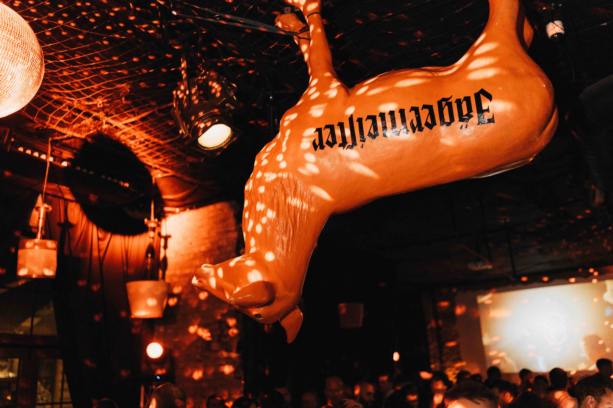 A large inflatable object hangs from the ceiling with the word "apopcia." The scene is dimly lit with red and orange lighting, and there are many people in the background, suggesting a lively event or party.