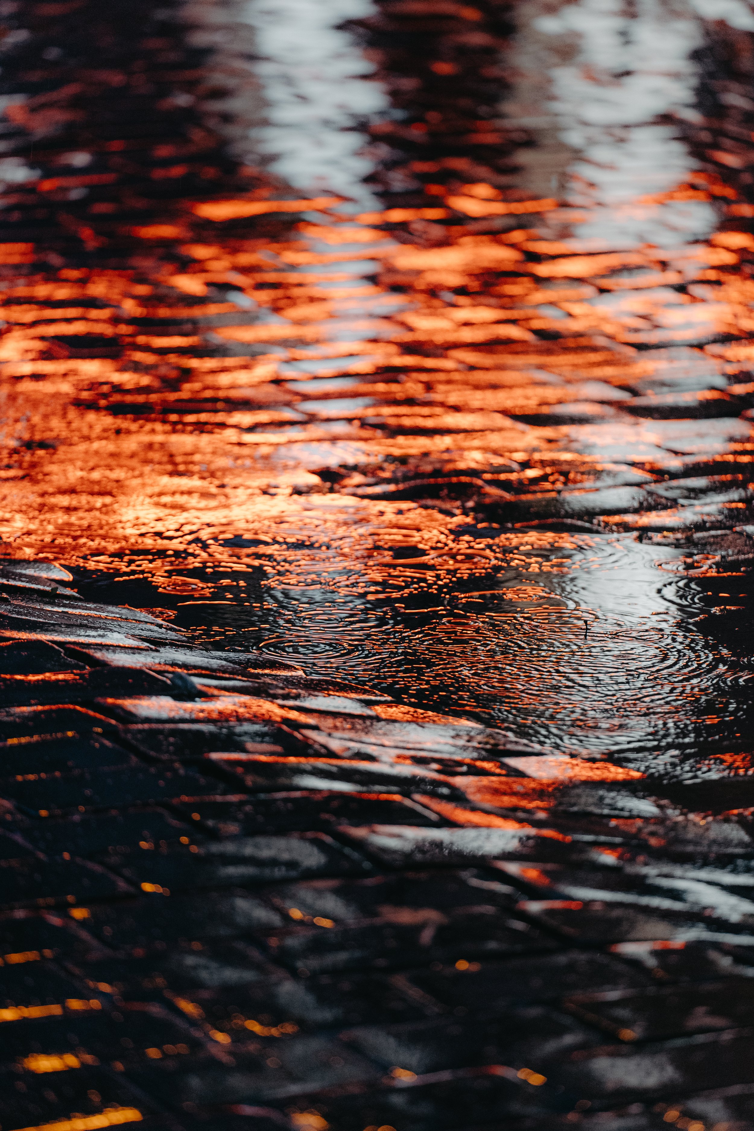 Reflection of warm orange and dark colors on wet cobblestone street.